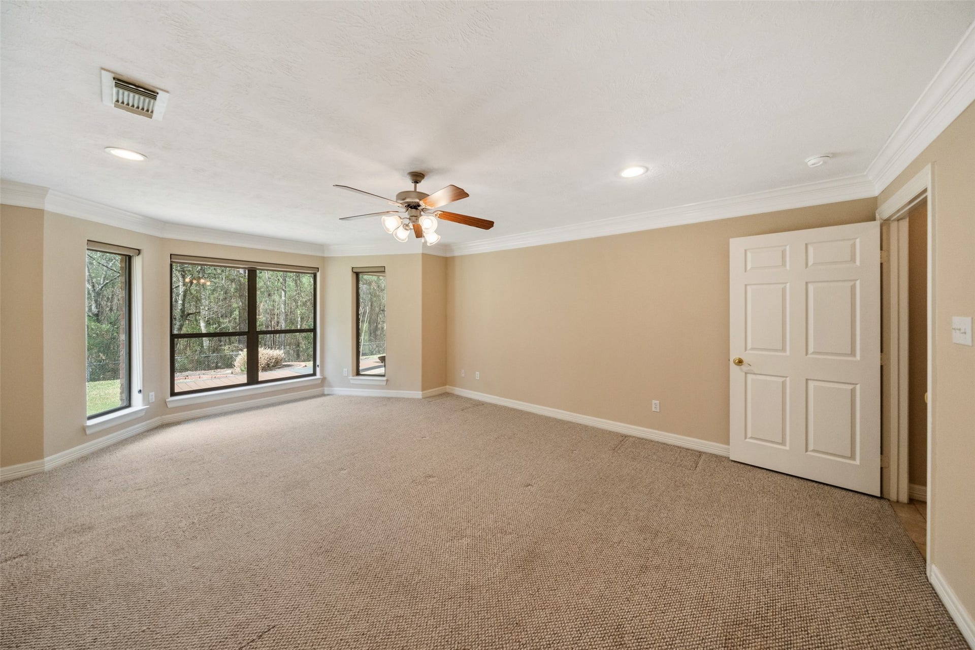 901 Longmire Road, #28, Conroe, TX 77304 First floor primary bedroom features neutral walls and carpet, large windows with views of greenery, and a ceiling fan with recess lights, creating a bright and inviting atmosphere.