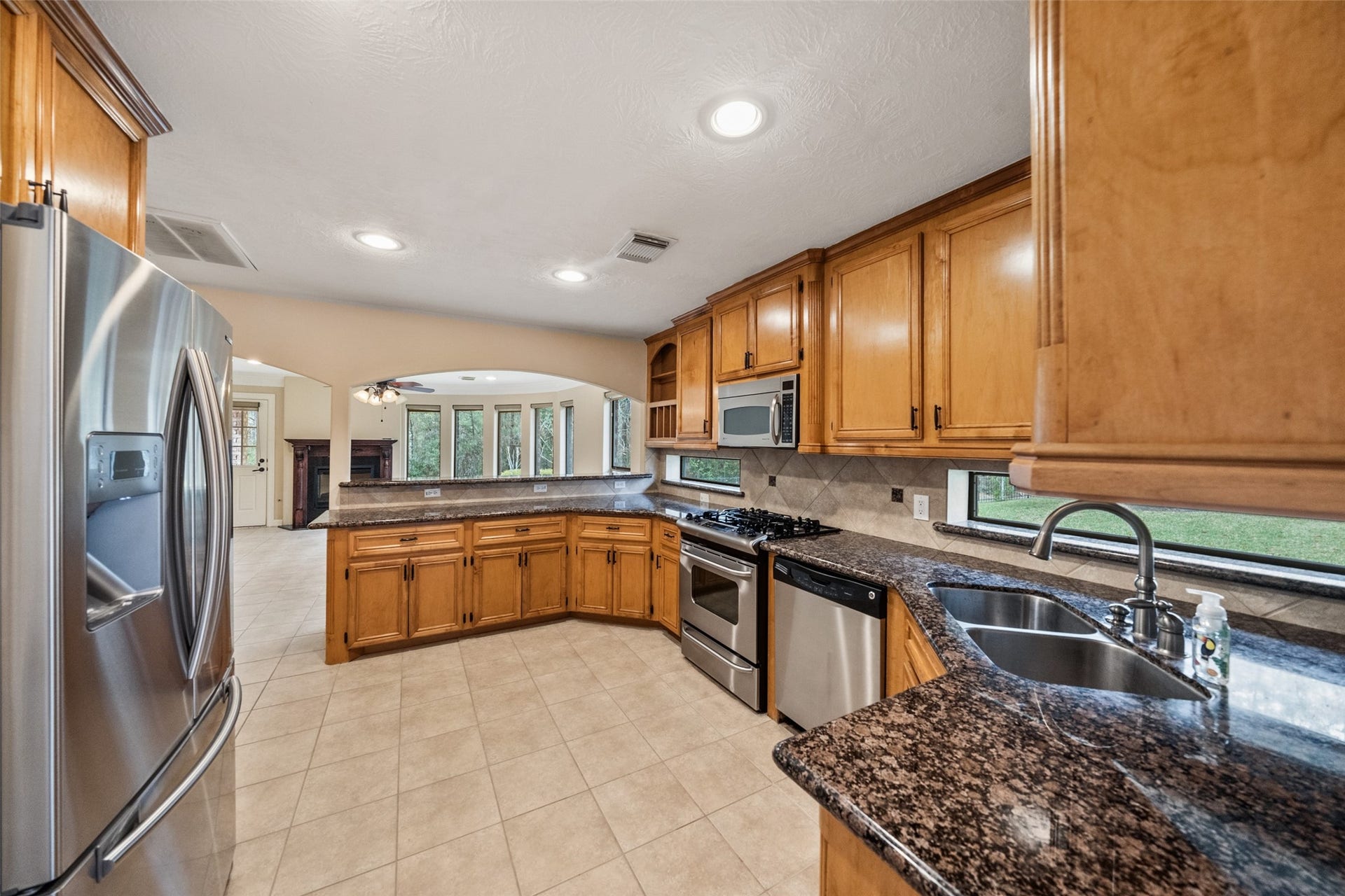 901 Longmire Road, #28, Conroe, TX 77304 Spacious kitchen with granite countertops, stainless steel appliances, and ample wooden cabinetry. It features a double sink, gas stove, and a view into a bright living area with large windows.