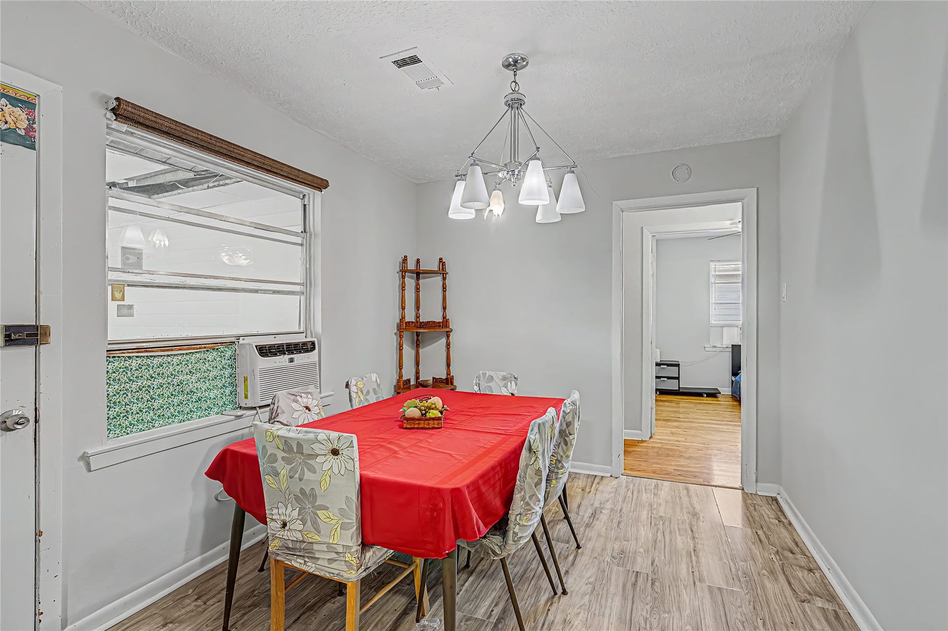 Bright dining area with modern chandelier adjacent to a cozy room with wooden flooring.