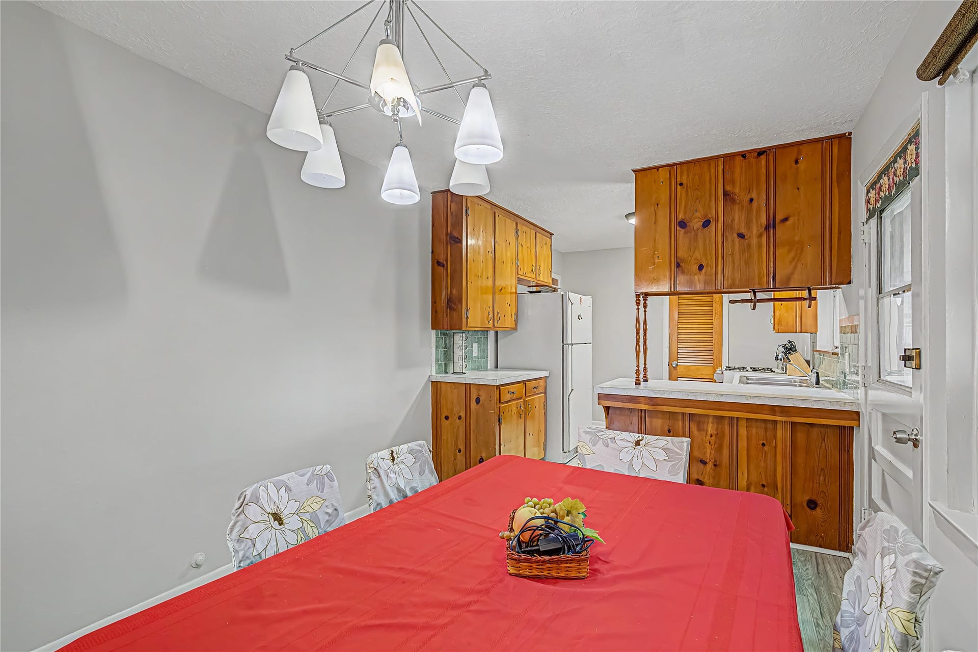 Charming dining area with a cozy kitchen featuring warm wood cabinetry, a stylish light fixture, and a vibrant table setting, perfect for family meals.
