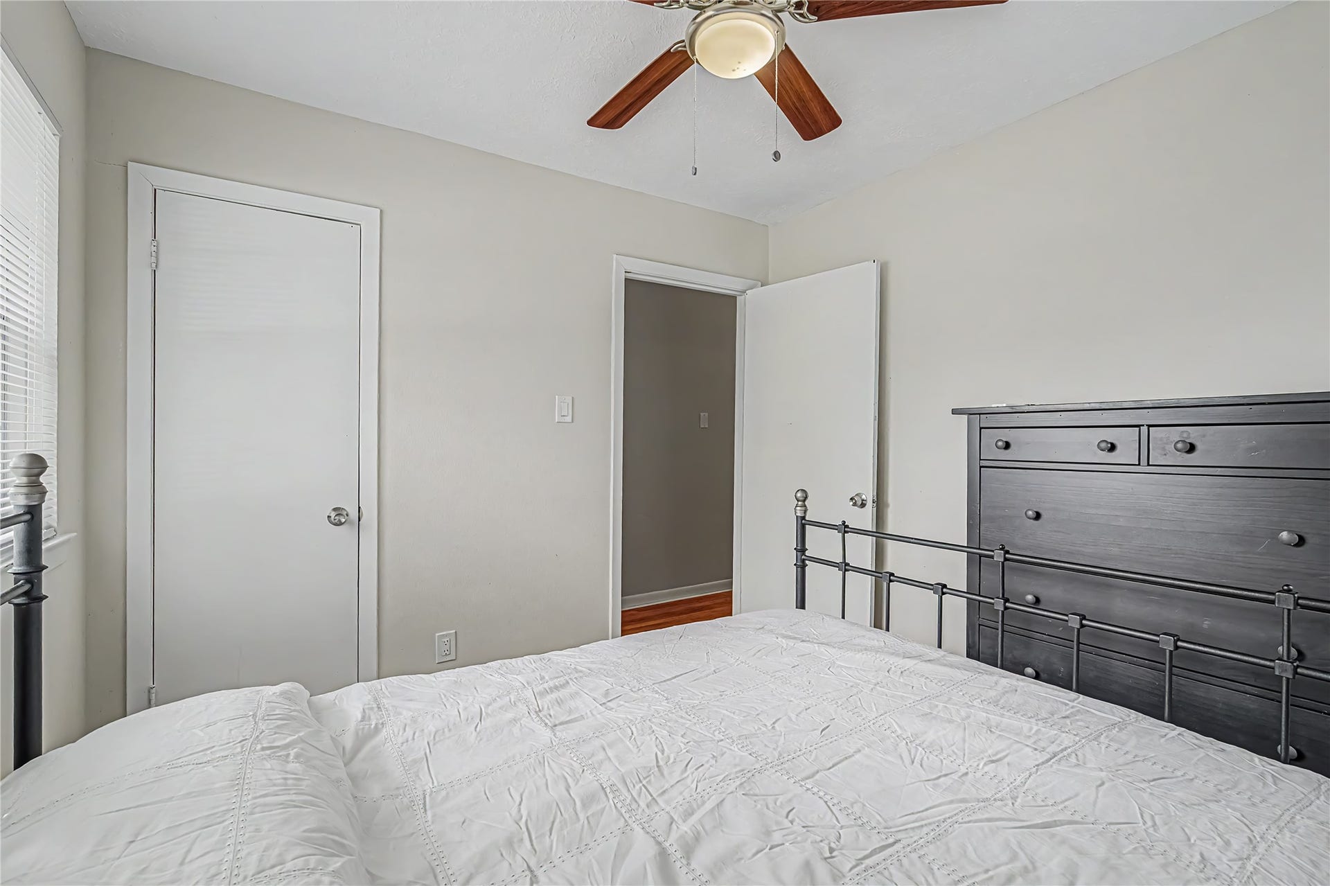 Cozy bedroom with a ceiling fan, neutral walls, and ample natural light, featuring a stylish black metal bed frame and matching dresser for a modern touch.