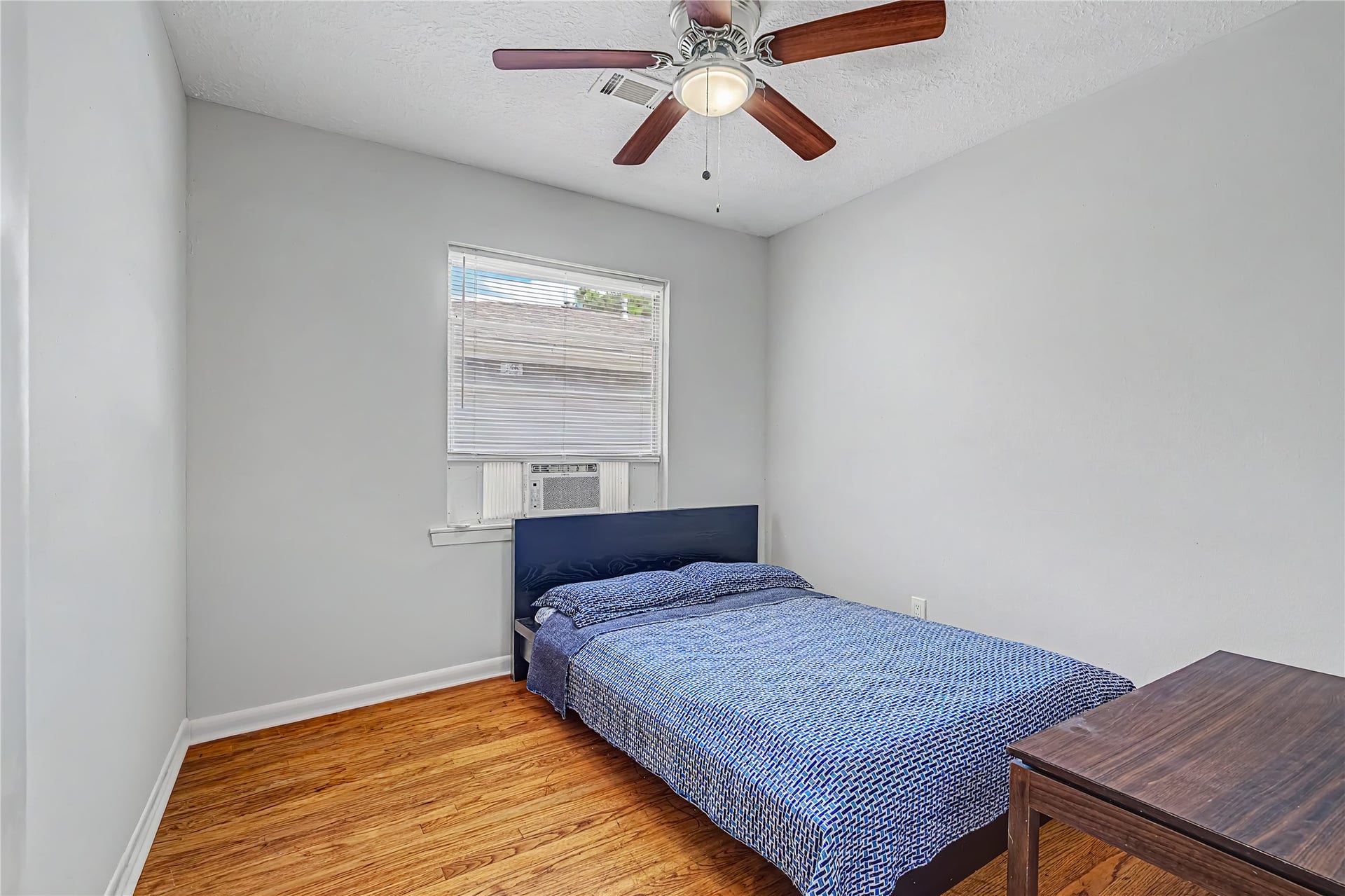 Cozy bedroom with hardwood floors, a ceiling fan, and natural light from a window, perfect for a restful retreat.