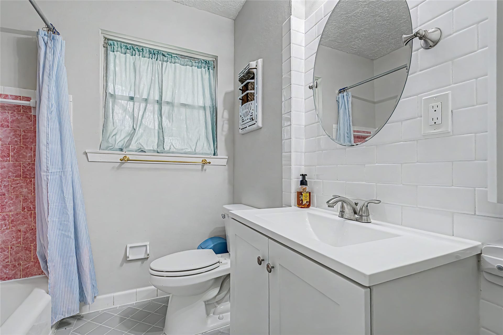 Charming bathroom featuring a modern vanity with a sleek round mirror, classic white subway tile, and a cozy tub.