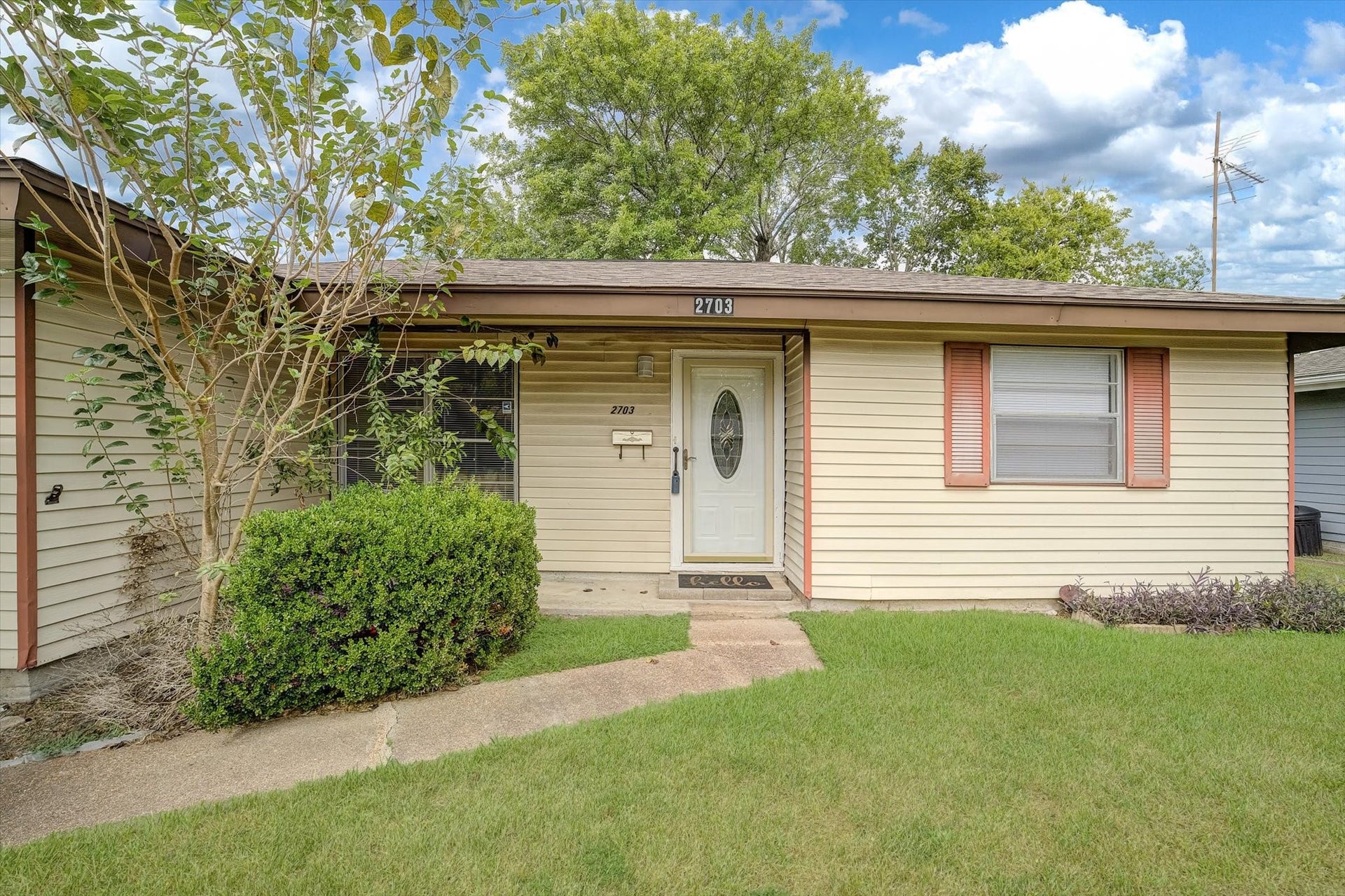 Charming single-story home with a welcoming front entrance, surrounded by lush greenery and mature trees, offering a cozy and inviting atmosphere.