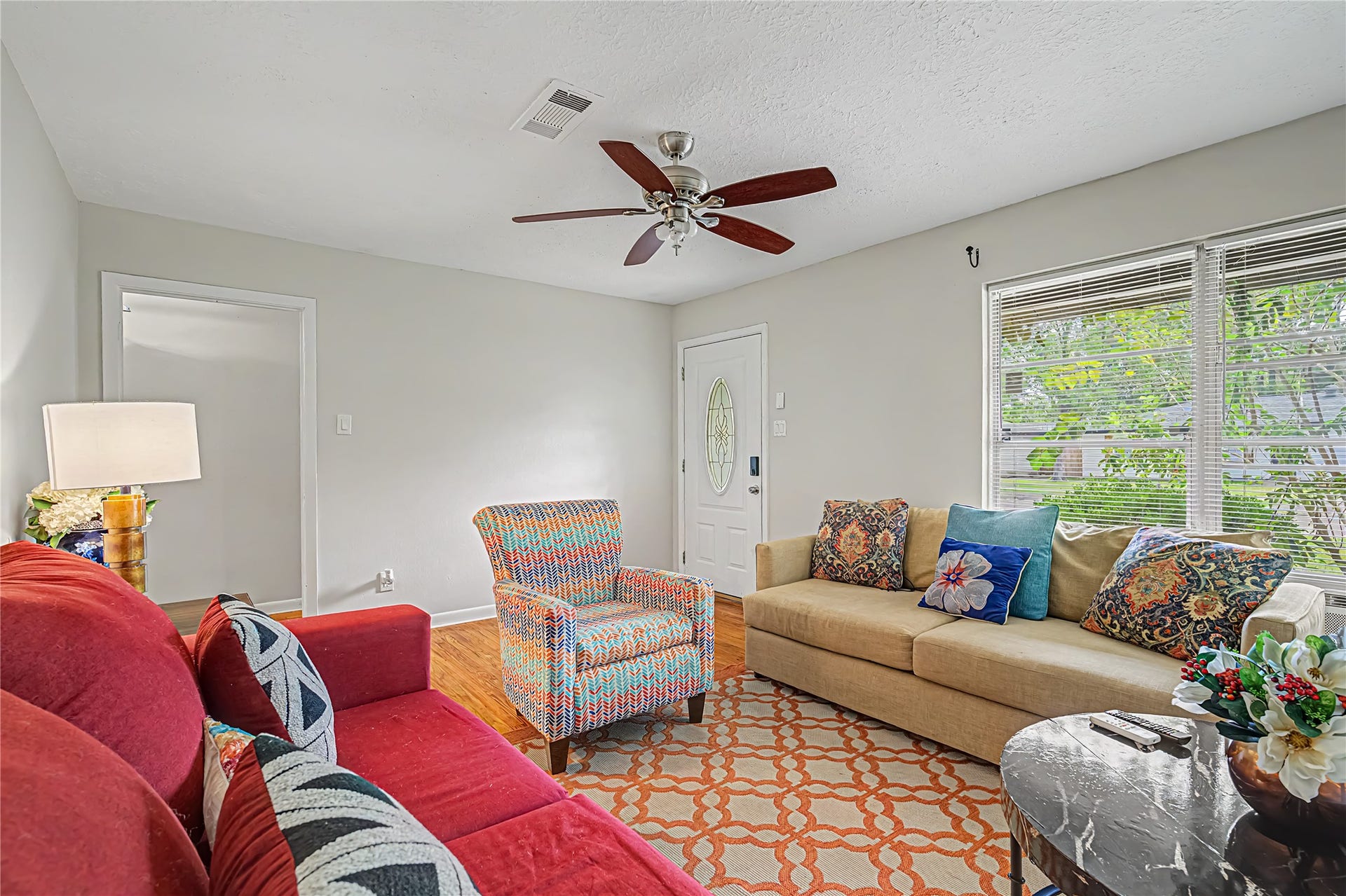 Cozy living room with vibrant seating, a ceiling fan, and ample natural light from large windows, creating a welcoming atmosphere.