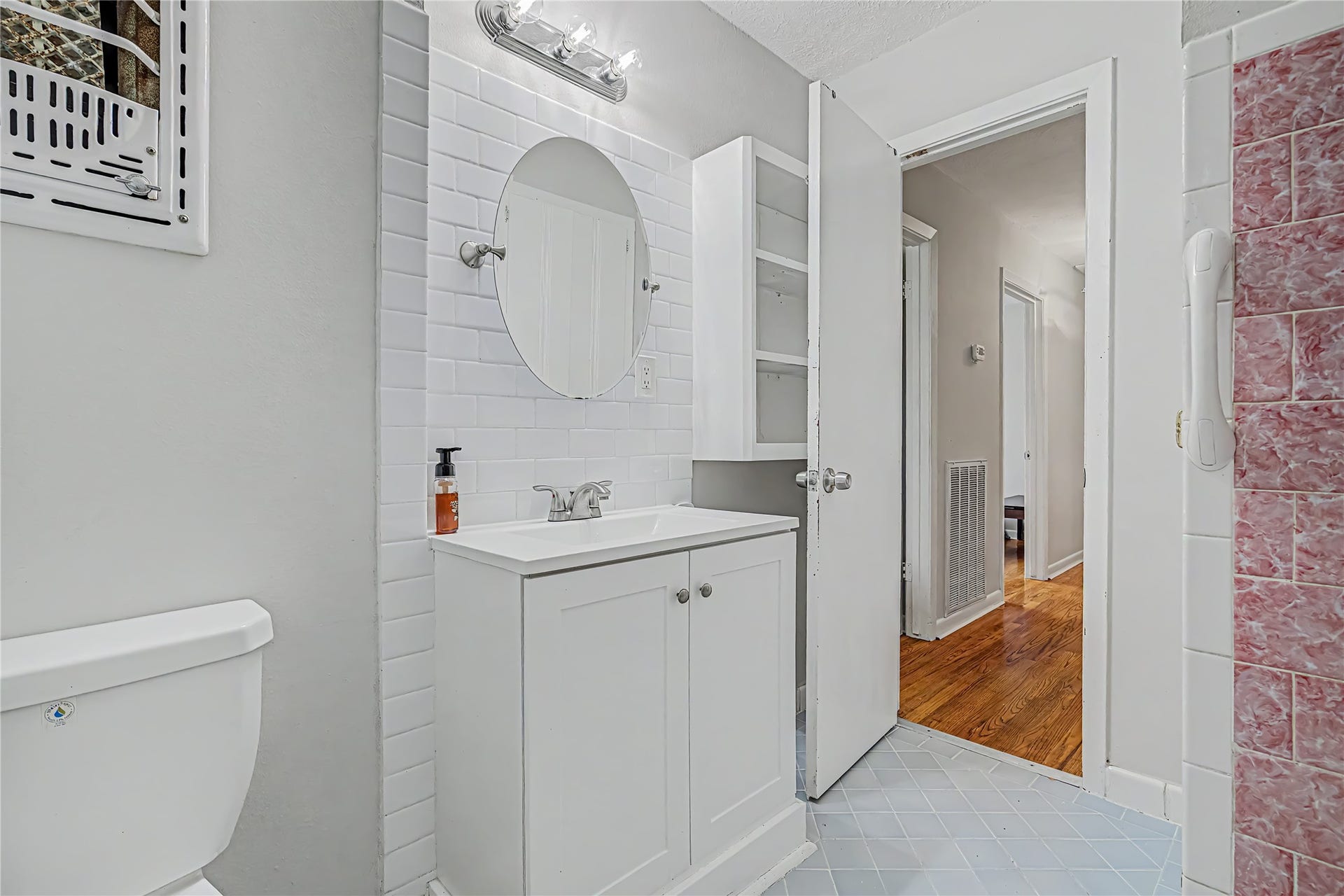 Bright bathroom featuring a modern vanity with a round mirror, white subway tile backsplash, and ample storage.