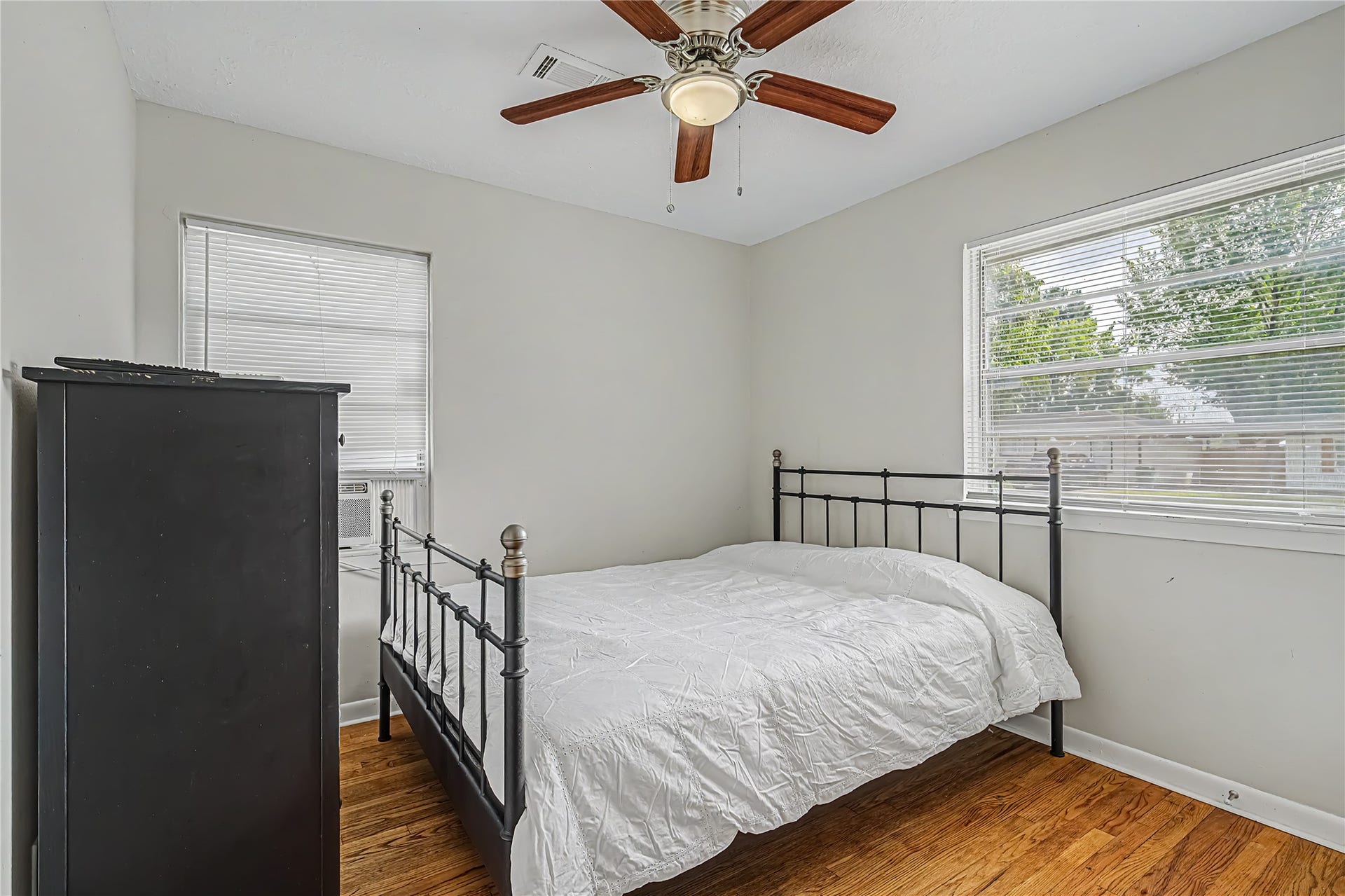Cozy bedroom featuring hardwood floors, a ceiling fan, and abundant natural light from two windows, creating a bright and inviting space.