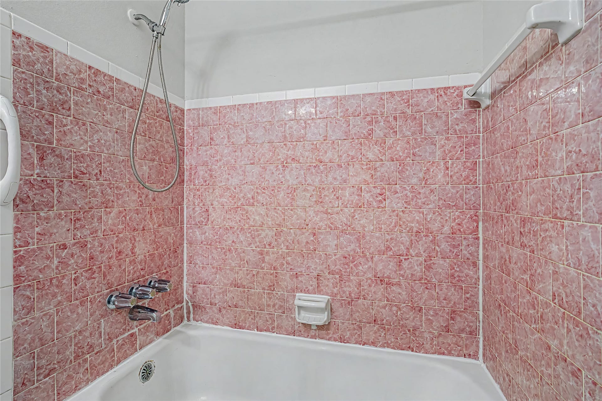 Charming bathroom with vintage pink tile accents and a classic white bathtub, perfect for a retro-inspired touch.