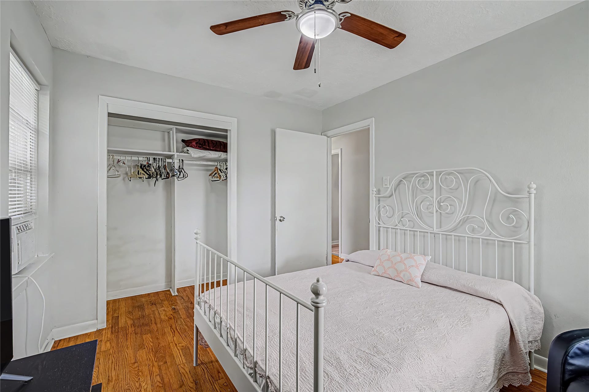 Charming bedroom with a stylish wrought iron bed, warm hardwood floors, and a ceiling fan for added comfort.