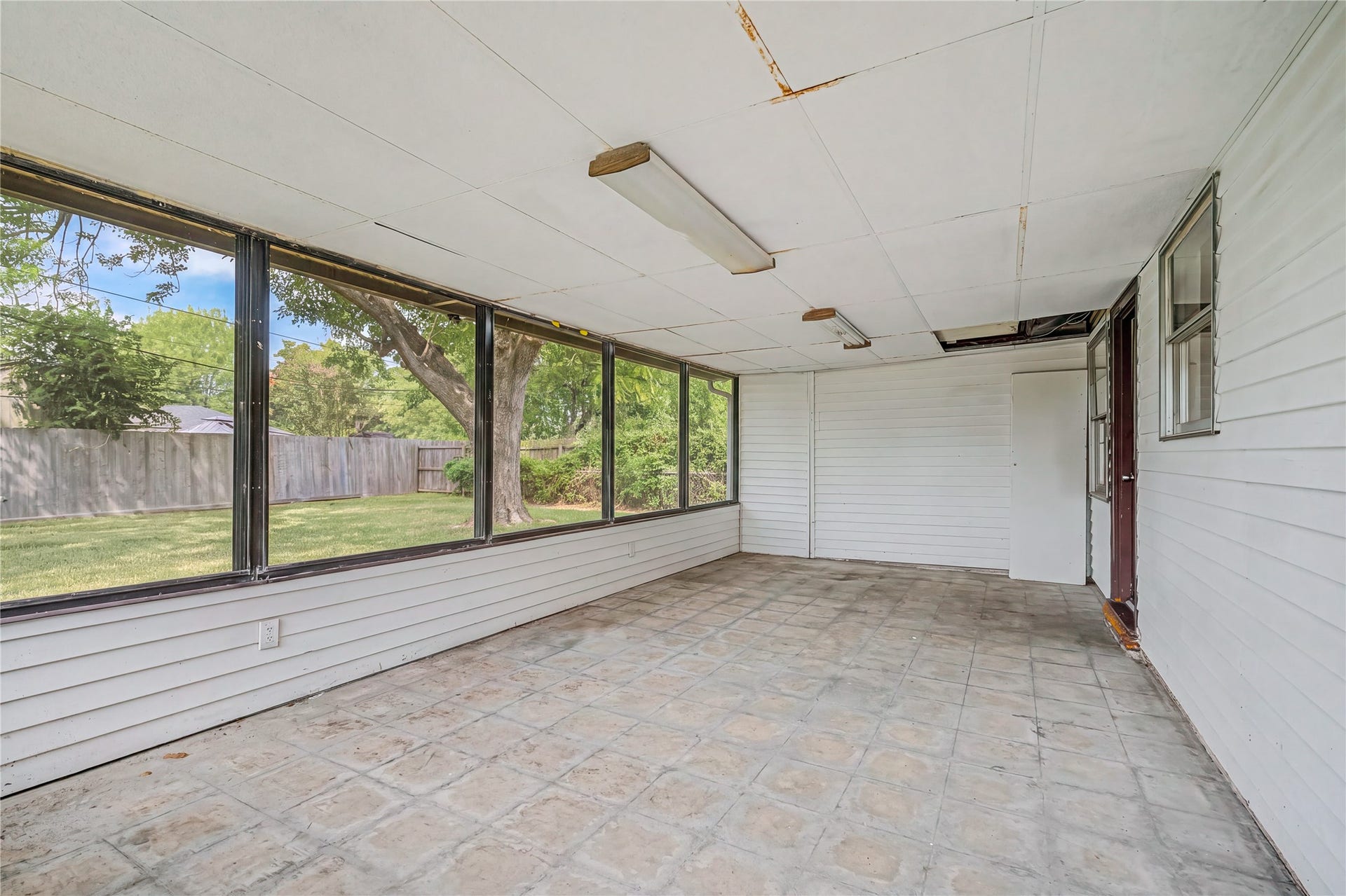 Spacious enclosed sunroom with large windows offering serene views of the lush backyard, perfect for relaxation or entertaining.