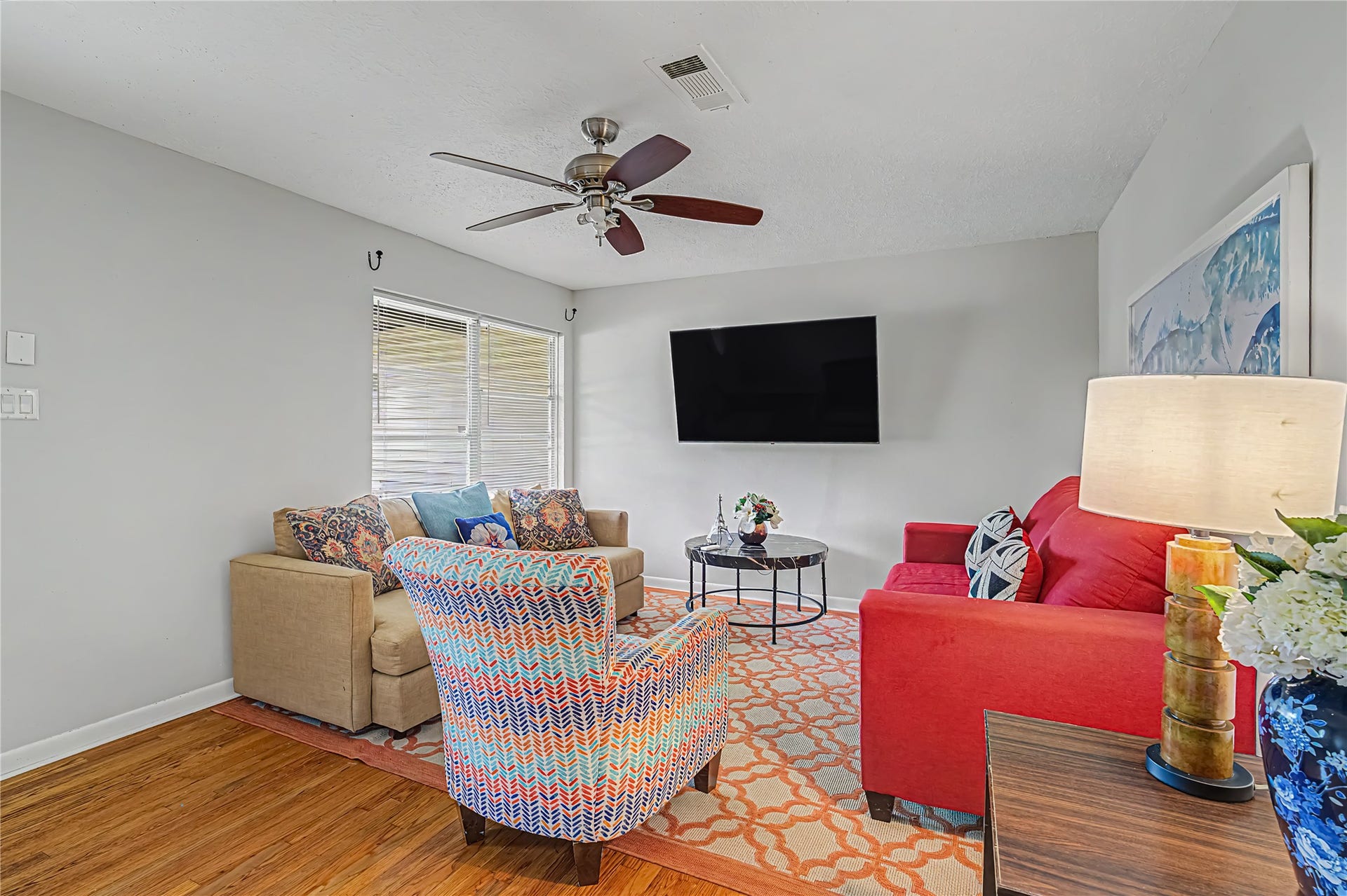 Cozy living room featuring vibrant seating, a large wall-mounted TV, and ample natural light, perfect for relaxing or entertaining.