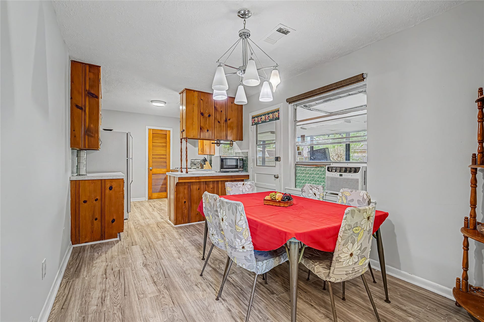 Charming dining area with modern light fixture, open to a cozy kitchen featuring warm wood cabinetry and laminate flooring.