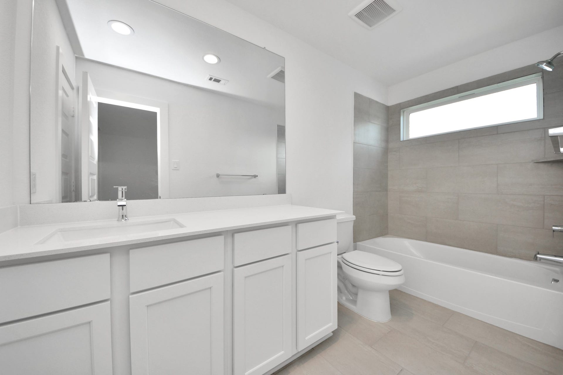 Secondary bath features tile flooring, bath/shower combo with tile surround, light stained wood cabinets, beautiful light countertop. Sample photo of completed home with similar floor plan. Actual colors and selections may vary.