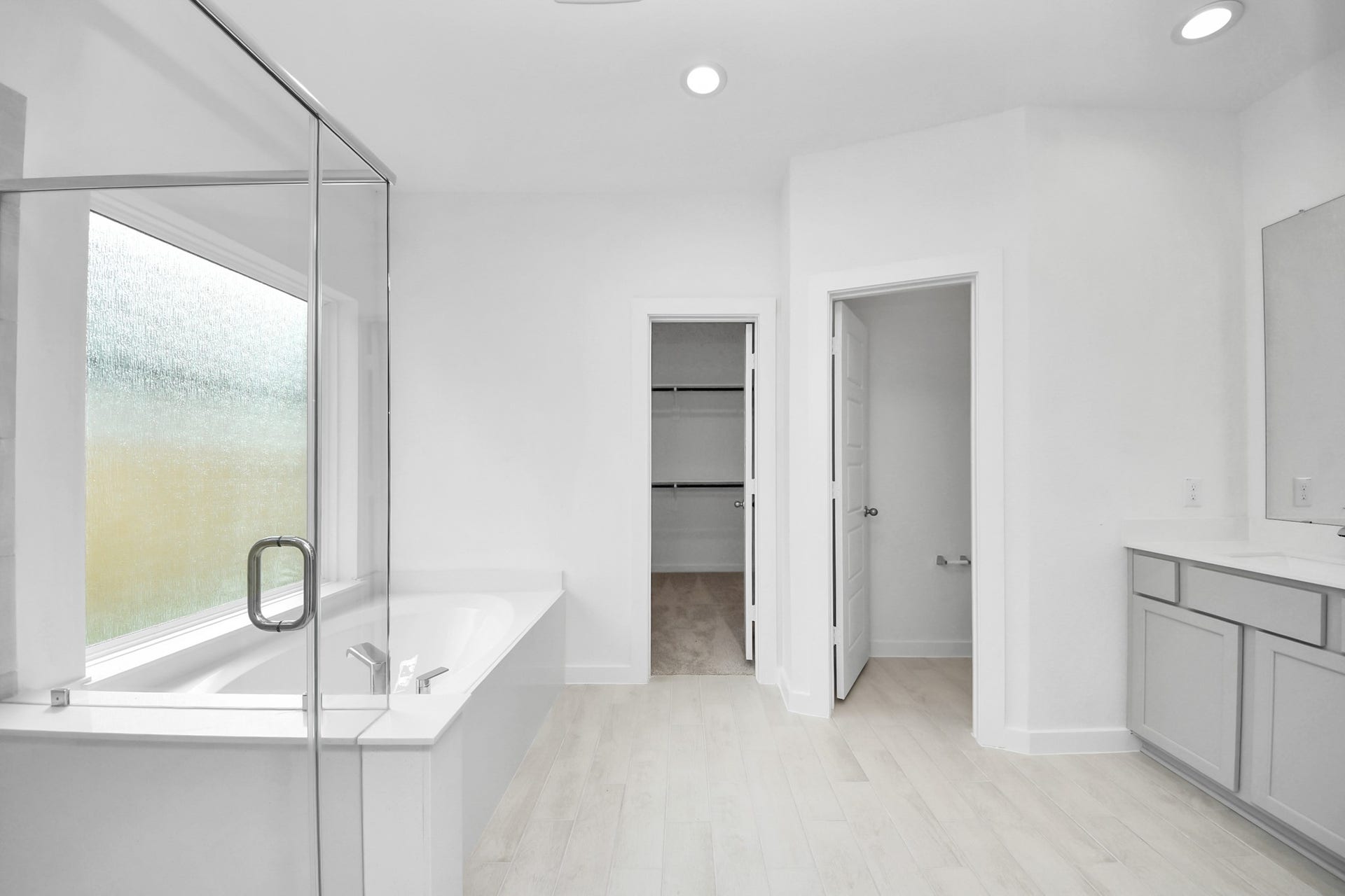 Escape to a spa-like oasis in this primary bathroom. Enjoy a walk-in shower with tile surround, a separate garden tub with custom detailing, and an elegant vanity featuring light countertops, modern hardware, and beautiful vanity lights. Experience luxury and relaxation in every detail. Sample photo of completed home with similar floor plan. Actual colors and selections may vary.