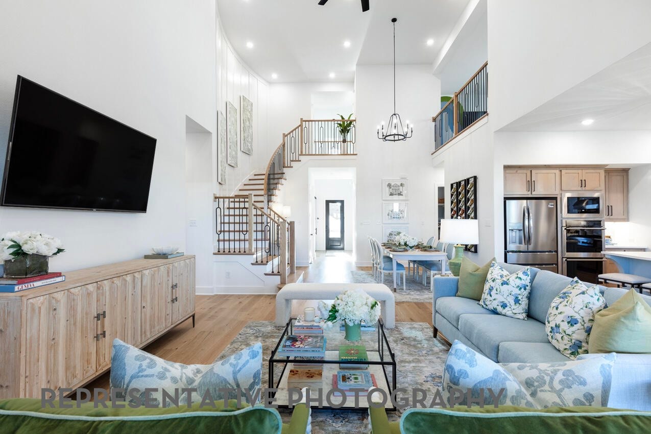Representative Photo- Grand family room featuring soaring ceilings, a dramatic staircase, and an open-concept layout.
