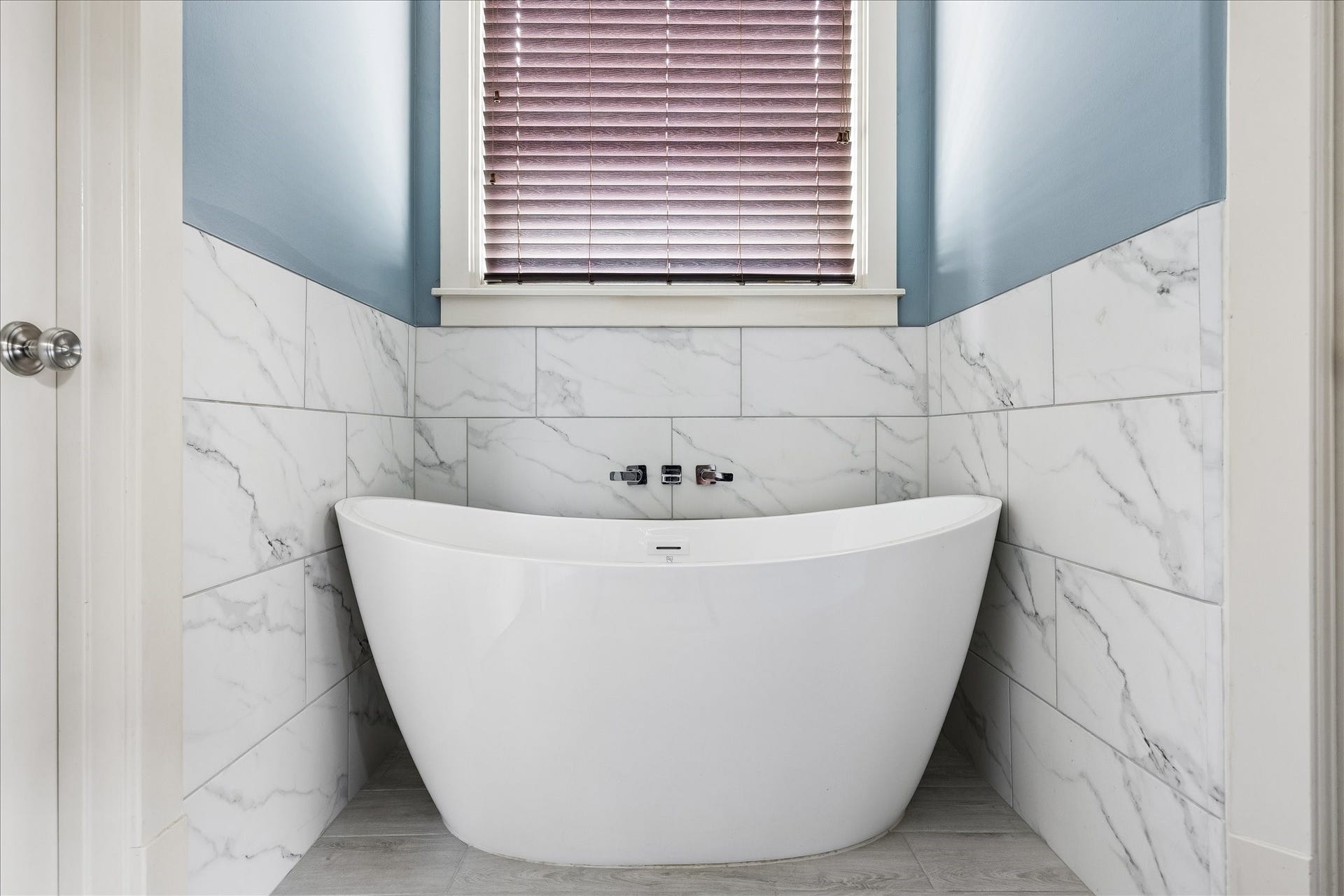 1332 W 21st Street, #B, Houston, TX 77008 A sculptural freestanding soaking tub takes center stage beneath the window, framed by soft blue walls and elegant tile.