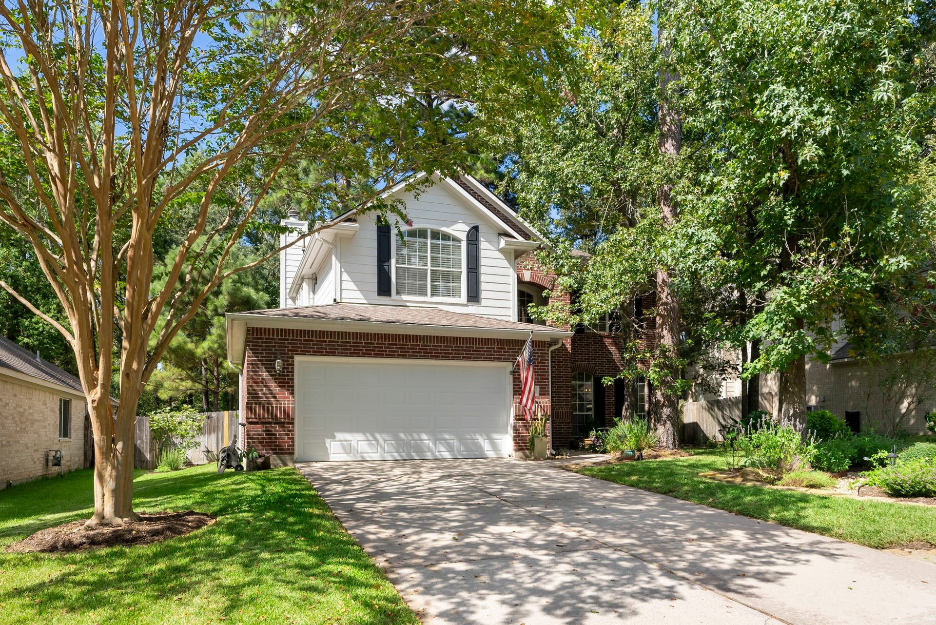 Charming two-story exterior tucked beneath mature shade trees, featuring classic brick accents, a welcoming front entry, and an attached two-car garage.