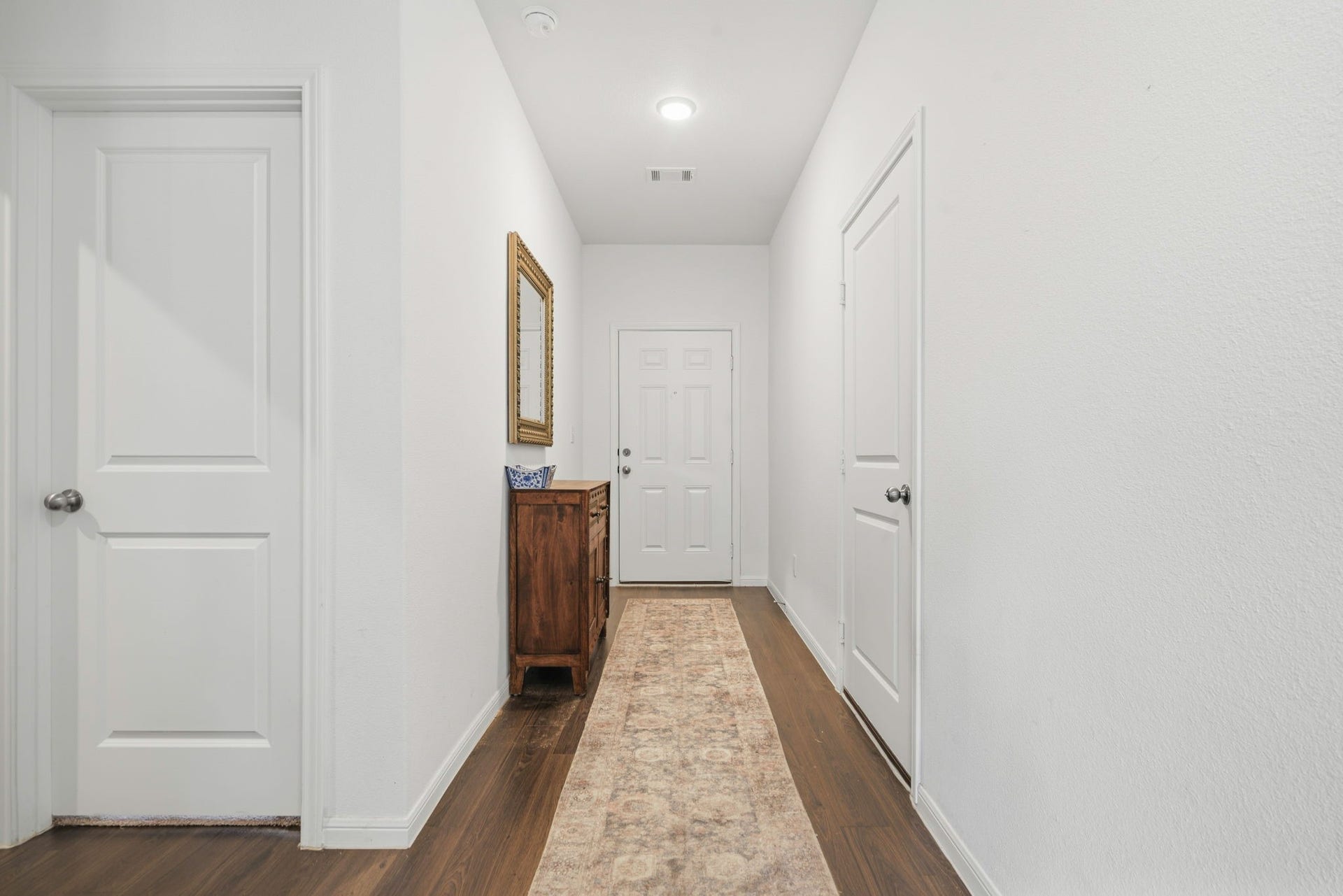 122 Ashwood Glade Lane, Conroe, TX 77378 Inviting hallway with rich wooden floors, elegant white doors, and a decorative mirror above a charming wooden cabinet.