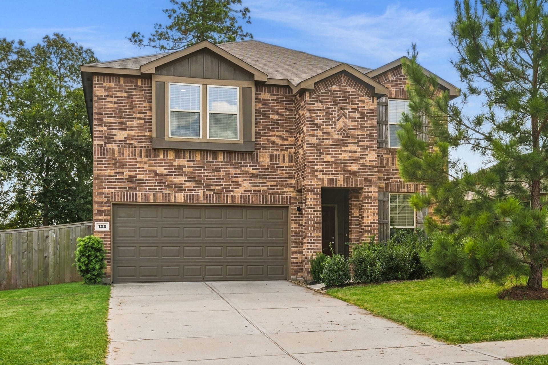122 Ashwood Glade Lane, Conroe, TX 77378 Charming two-story brick home featuring a spacious driveway, two-car garage, and lush landscaping, nestled in a serene neighborhood setting.