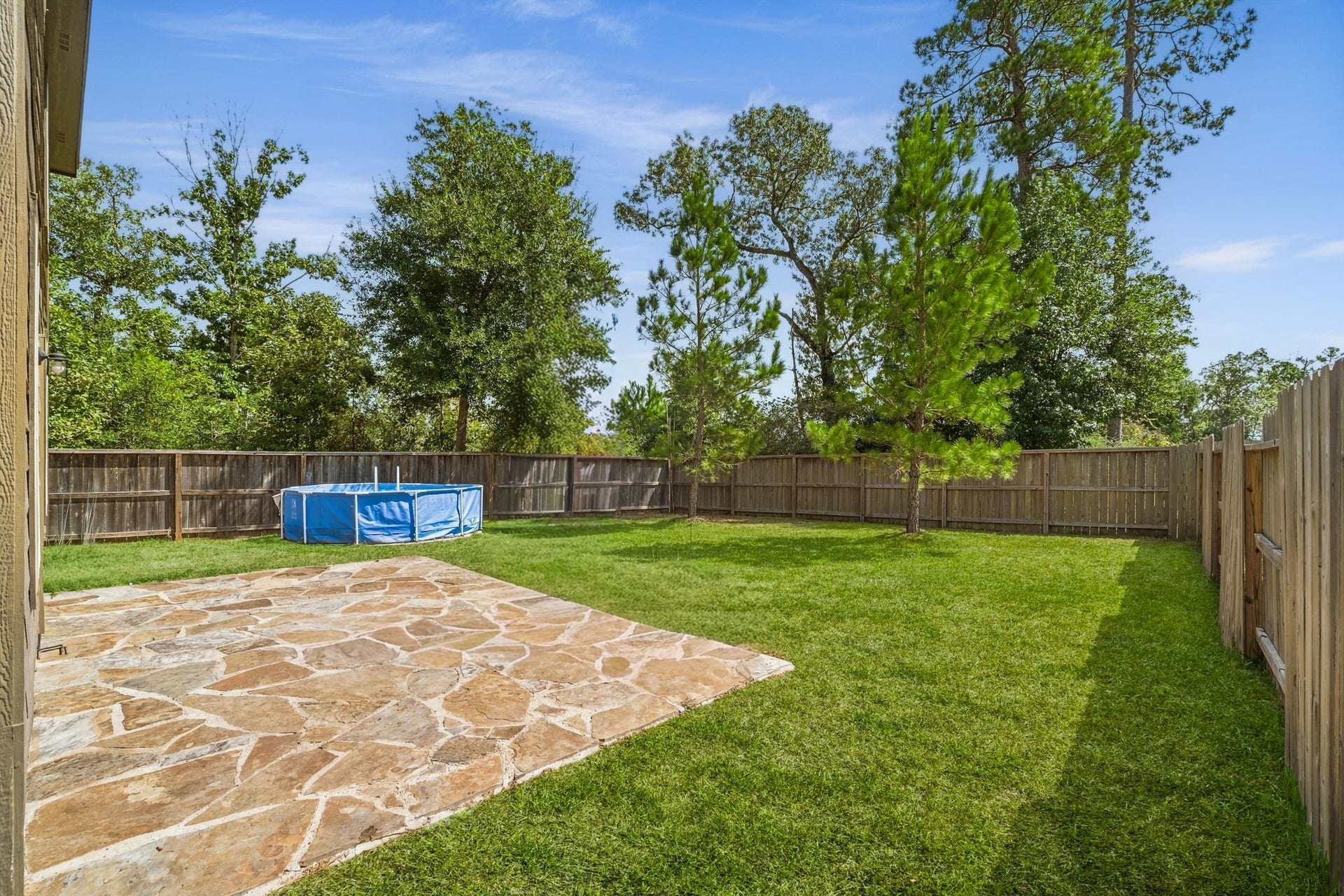 122 Ashwood Glade Lane, Conroe, TX 77378 Spacious backyard with a stone patio, lush lawn, privacy fence, and the above ground pool will be removed, perfect for outdoor enjoyment and relaxation.