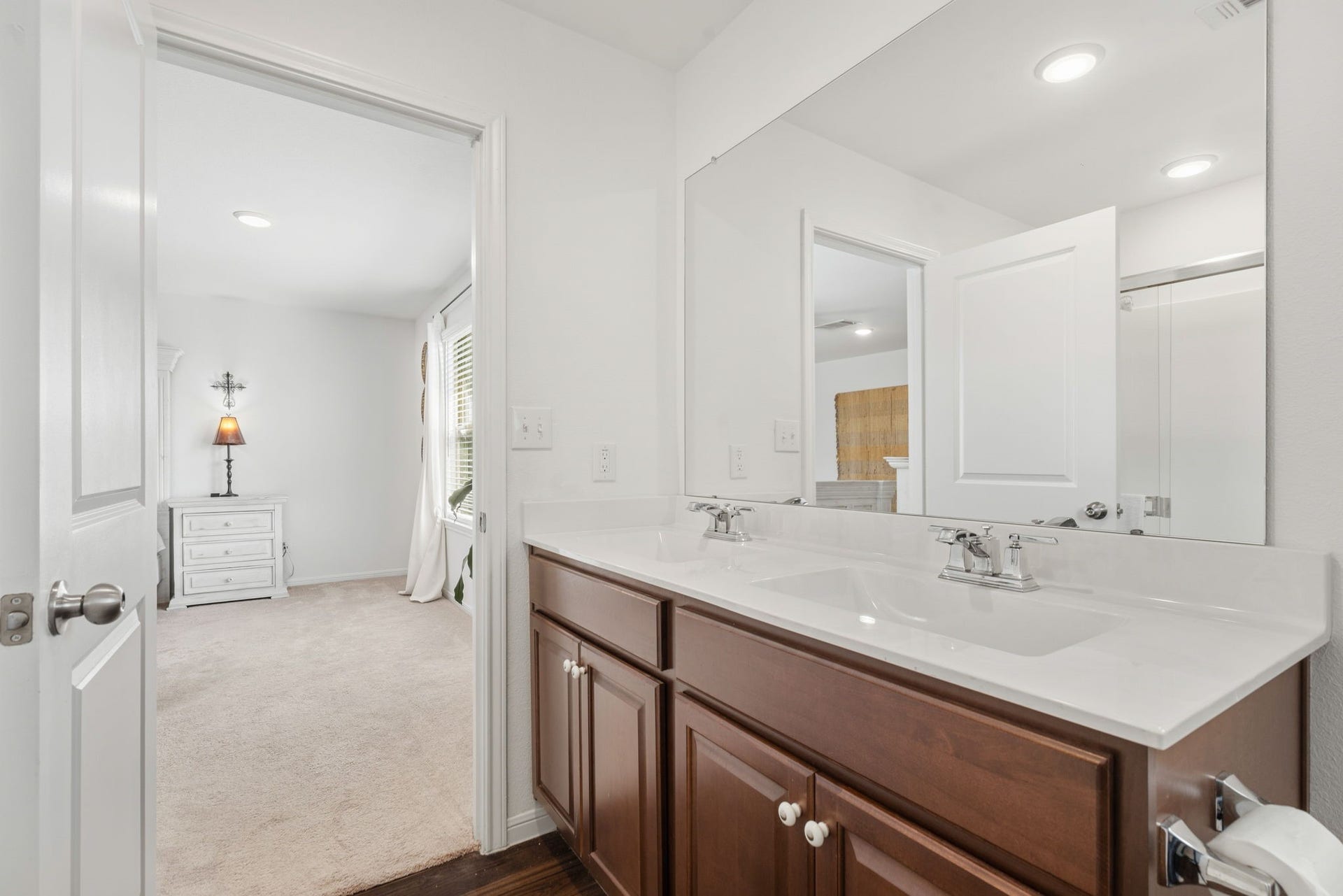 122 Ashwood Glade Lane, Conroe, TX 77378 Bright and inviting bathroom featuring a dual-sink vanity with elegant wood cabinetry, seamlessly connecting to a cozy, well-lit bedroom.