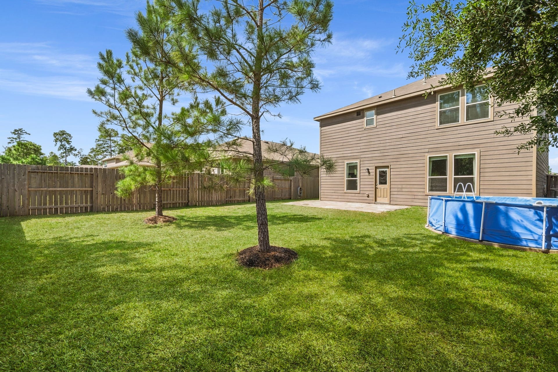 122 Ashwood Glade Lane, Conroe, TX 77378 Spacious backyard features lush green grass, trees, a fenced perimeter for privacy, and an above-ground pool will be removed.