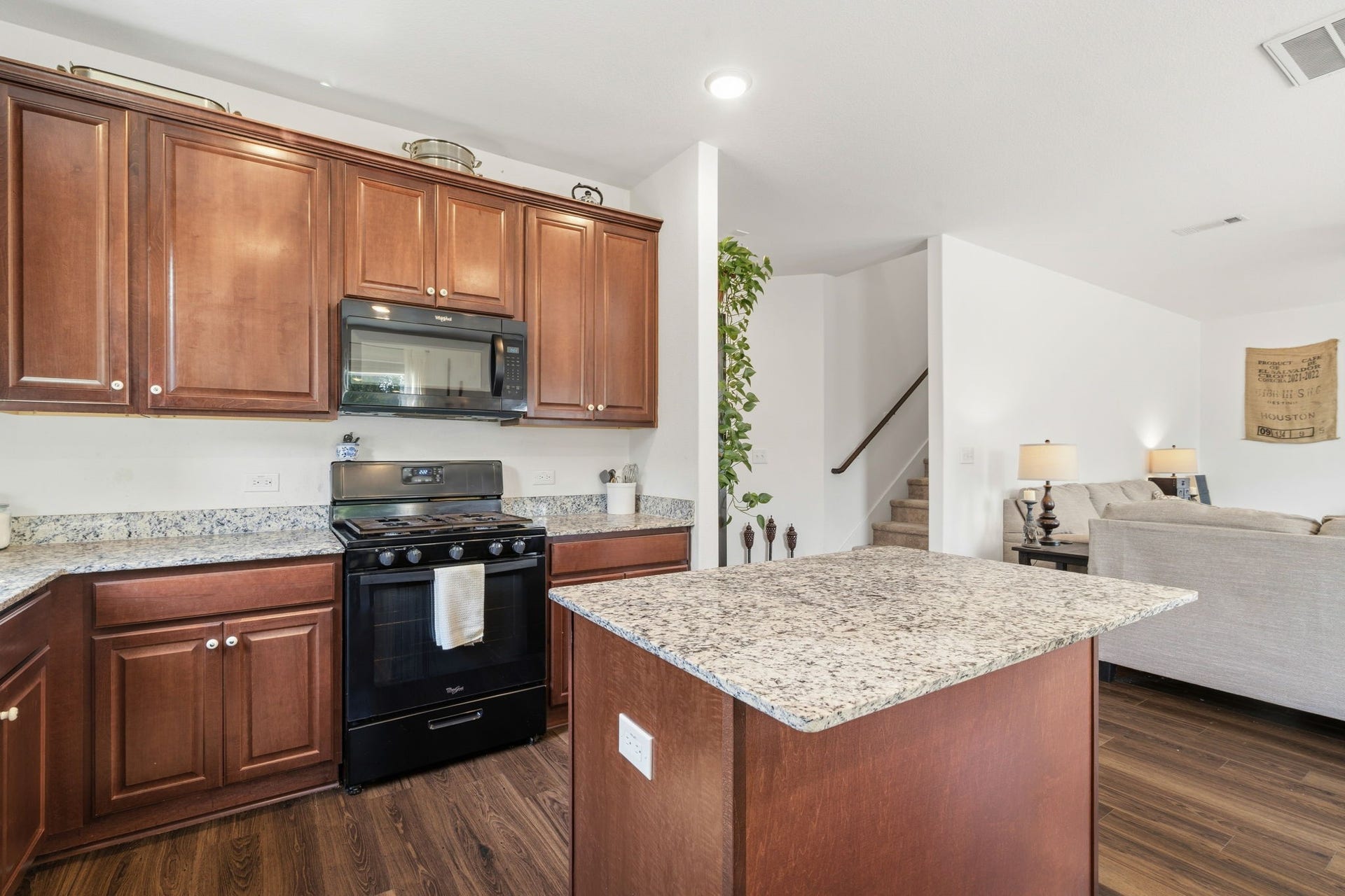 122 Ashwood Glade Lane, Conroe, TX 77378 Elegant kitchen with rich wood cabinetry, granite countertops, and a modern gas stove, seamlessly connecting to a cozy living area with plush seating and ambient lighting.