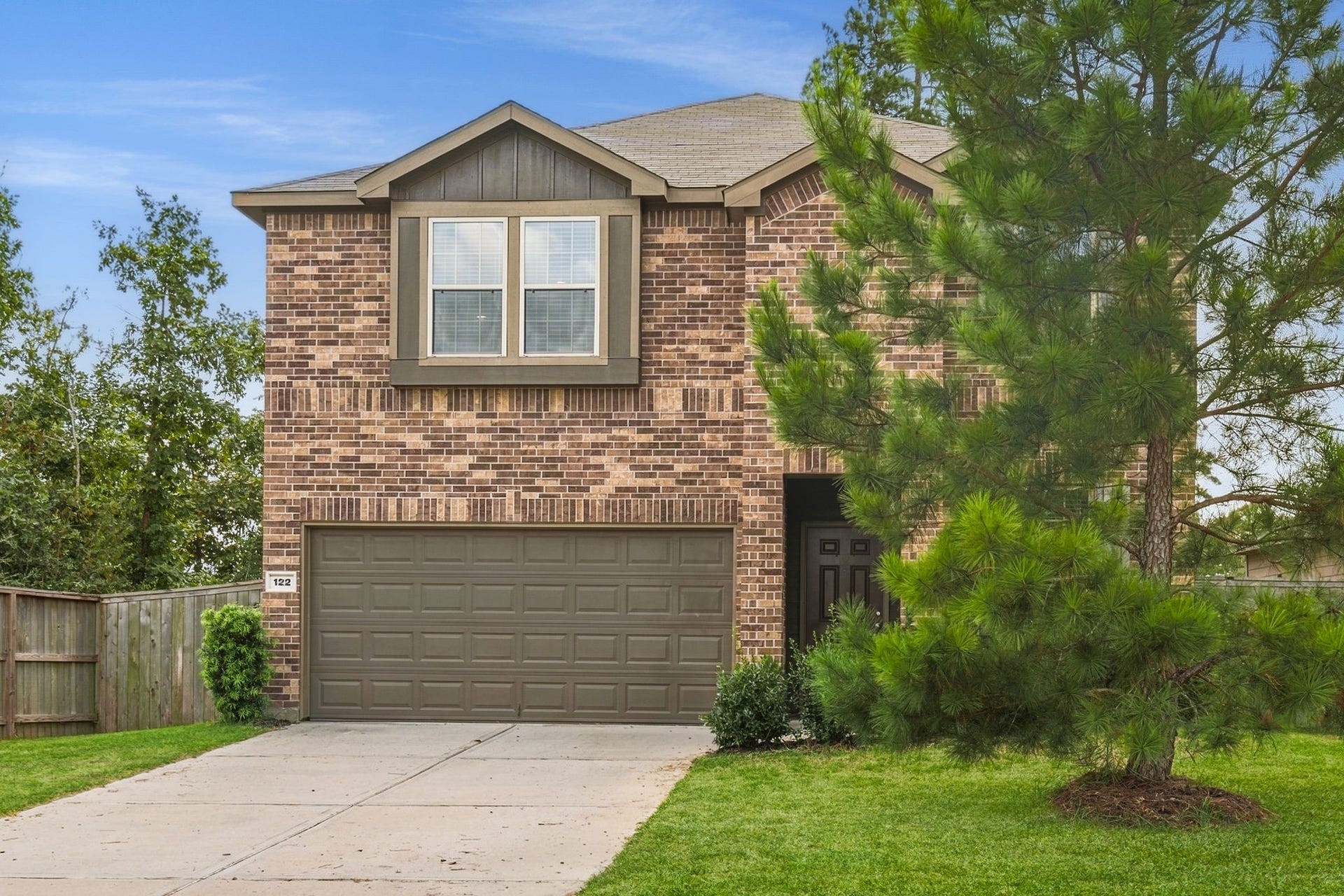 122 Ashwood Glade Lane, Conroe, TX 77378 Charming two-story brick home featuring a double garage, lush greenery, and a spacious front yard.