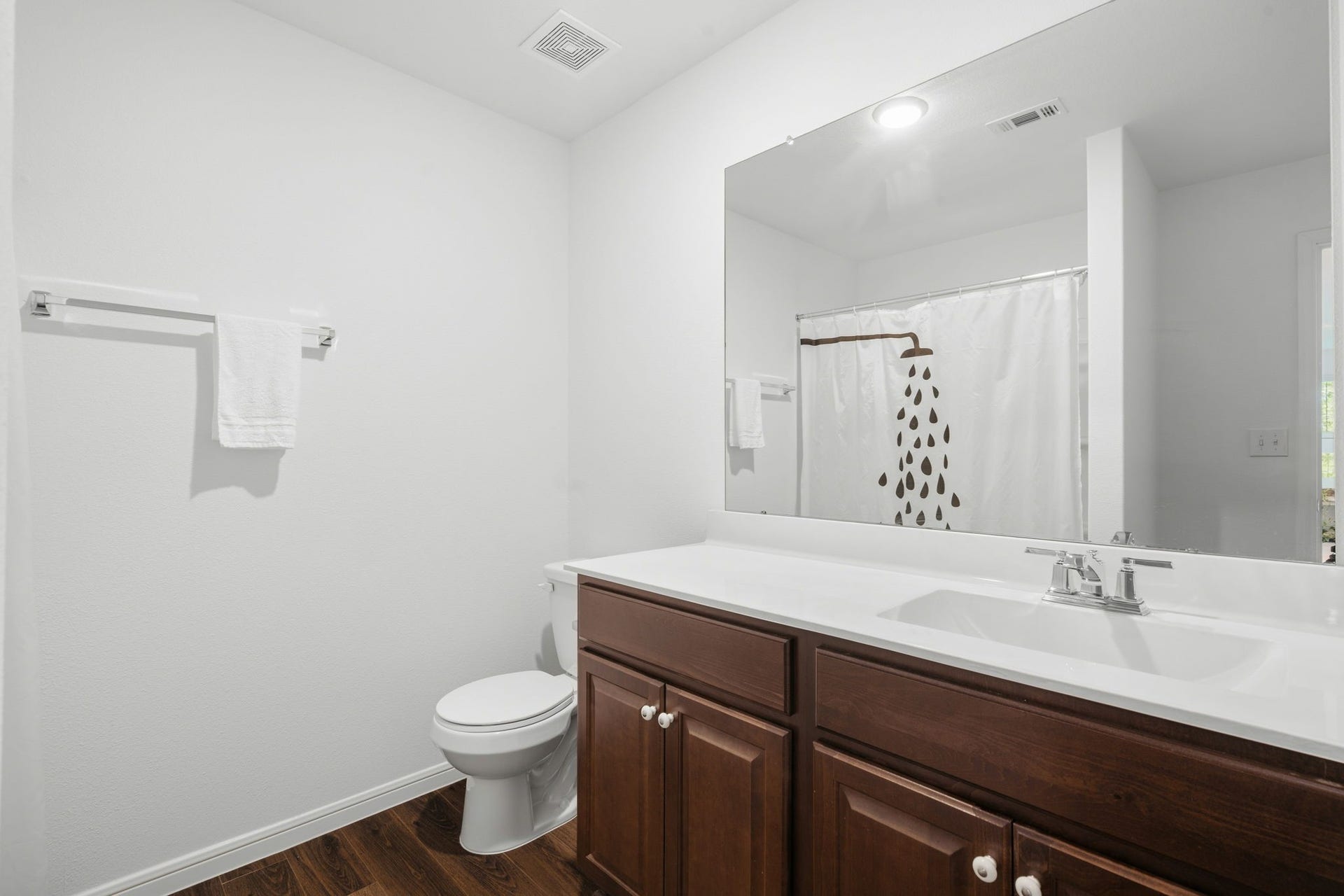 122 Ashwood Glade Lane, Conroe, TX 77378 Bright and inviting bathroom featuring a spacious vanity with rich wood cabinetry, a large mirror, and a stylish shower area with a playful curtain design.