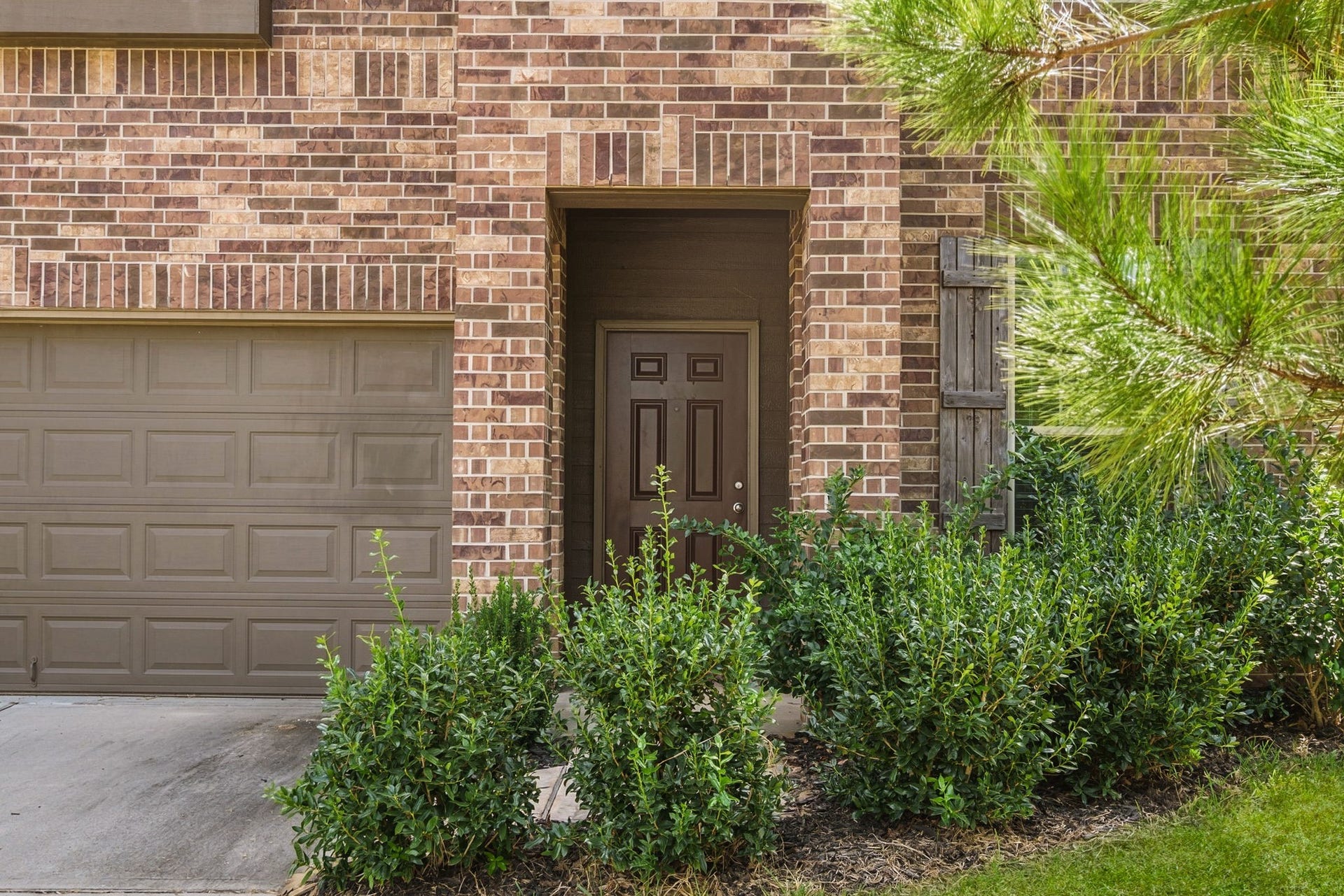 122 Ashwood Glade Lane, Conroe, TX 77378 Charming brick exterior featuring a cozy front entrance framed by lush greenery, alongside a convenient attached garage.