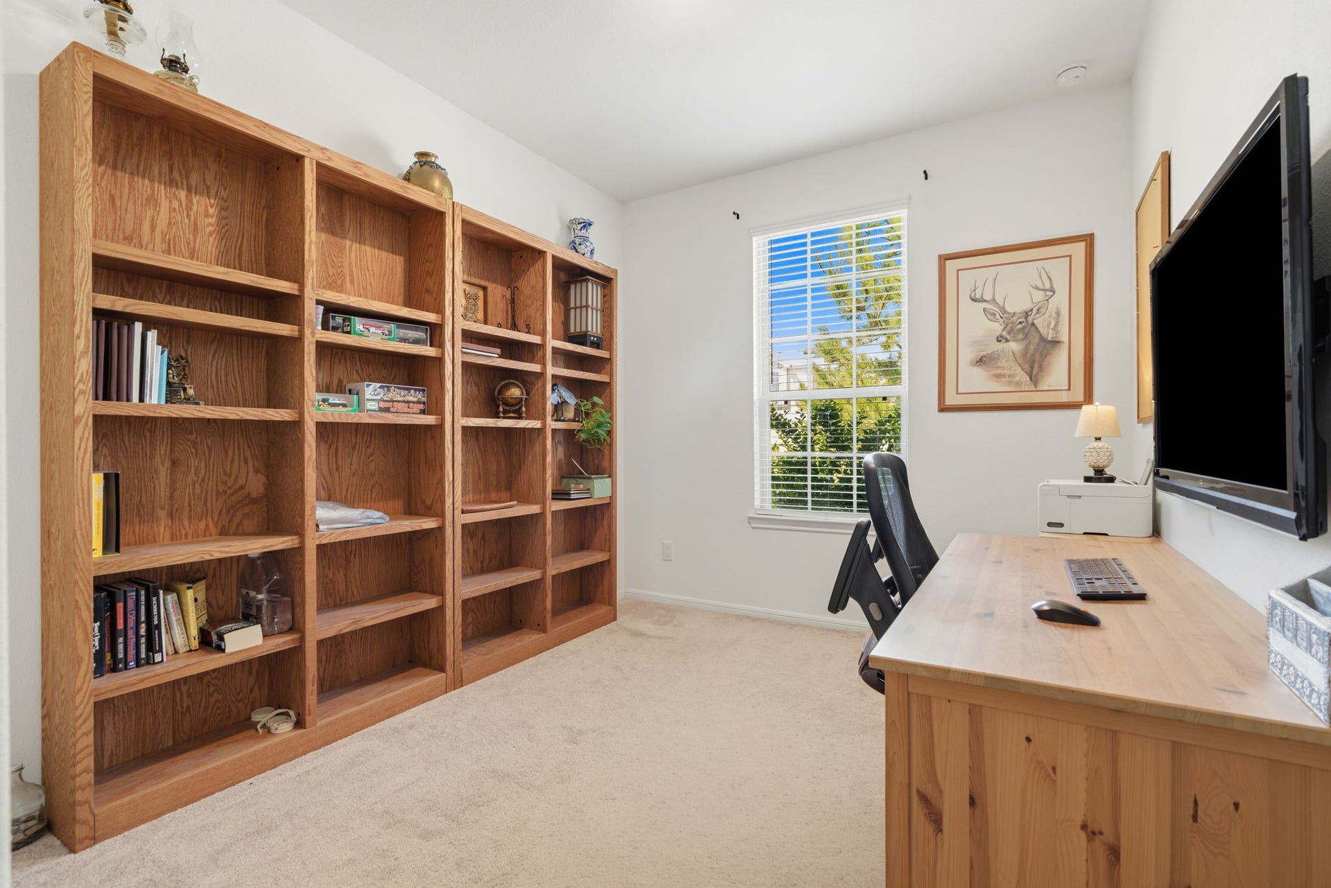 122 Ashwood Glade Lane, Conroe, TX 77378 Bright and inviting home office featuring a large wooden bookshelf, ample natural light through a window, and a functional desk space with a wall-mounted TV.