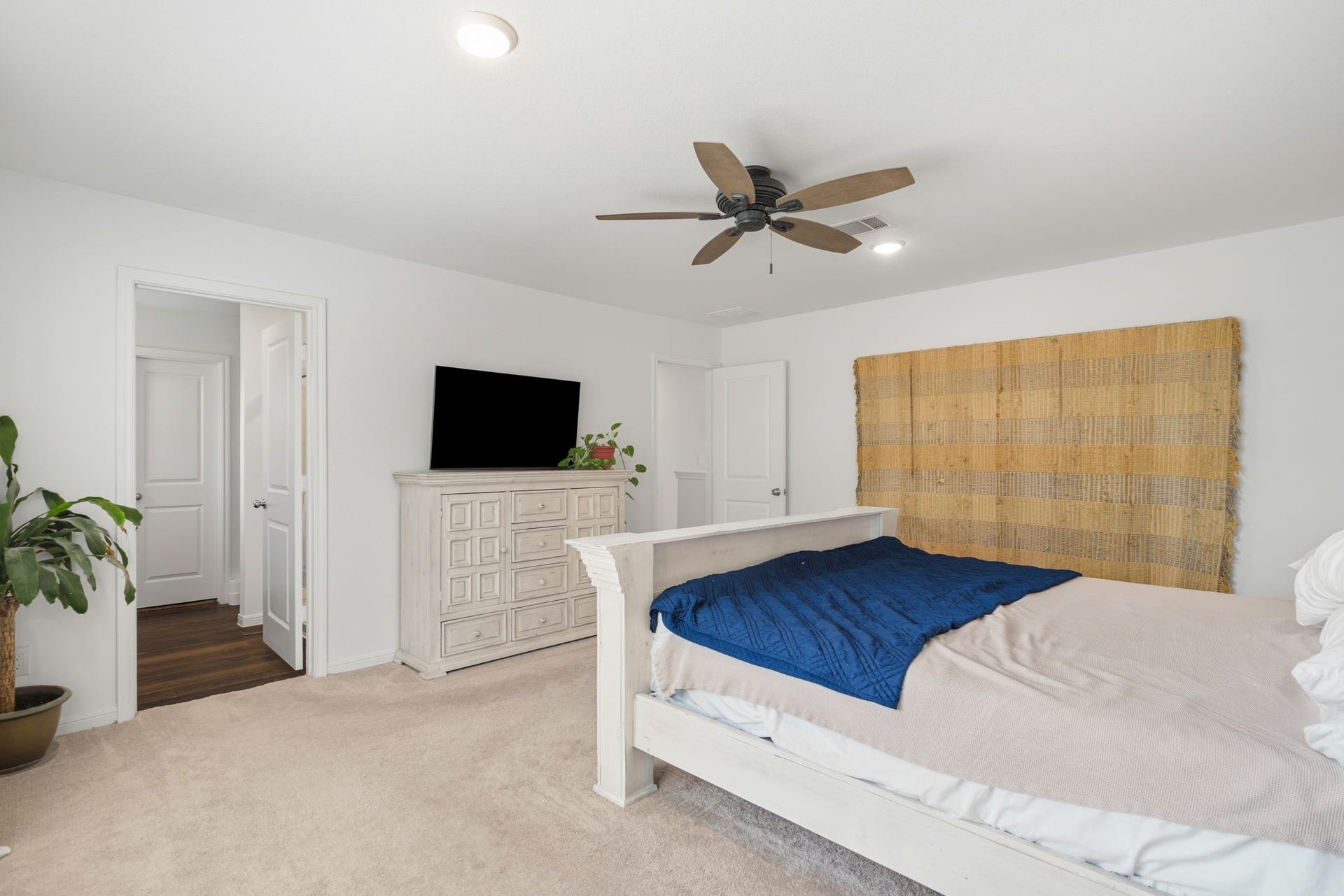 122 Ashwood Glade Lane, Conroe, TX 77378 Spacious bedroom with a cozy carpet, modern ceiling fan, and ample natural light. Features a stylish dresser, TV, and decorative wall hanging, creating a serene retreat.