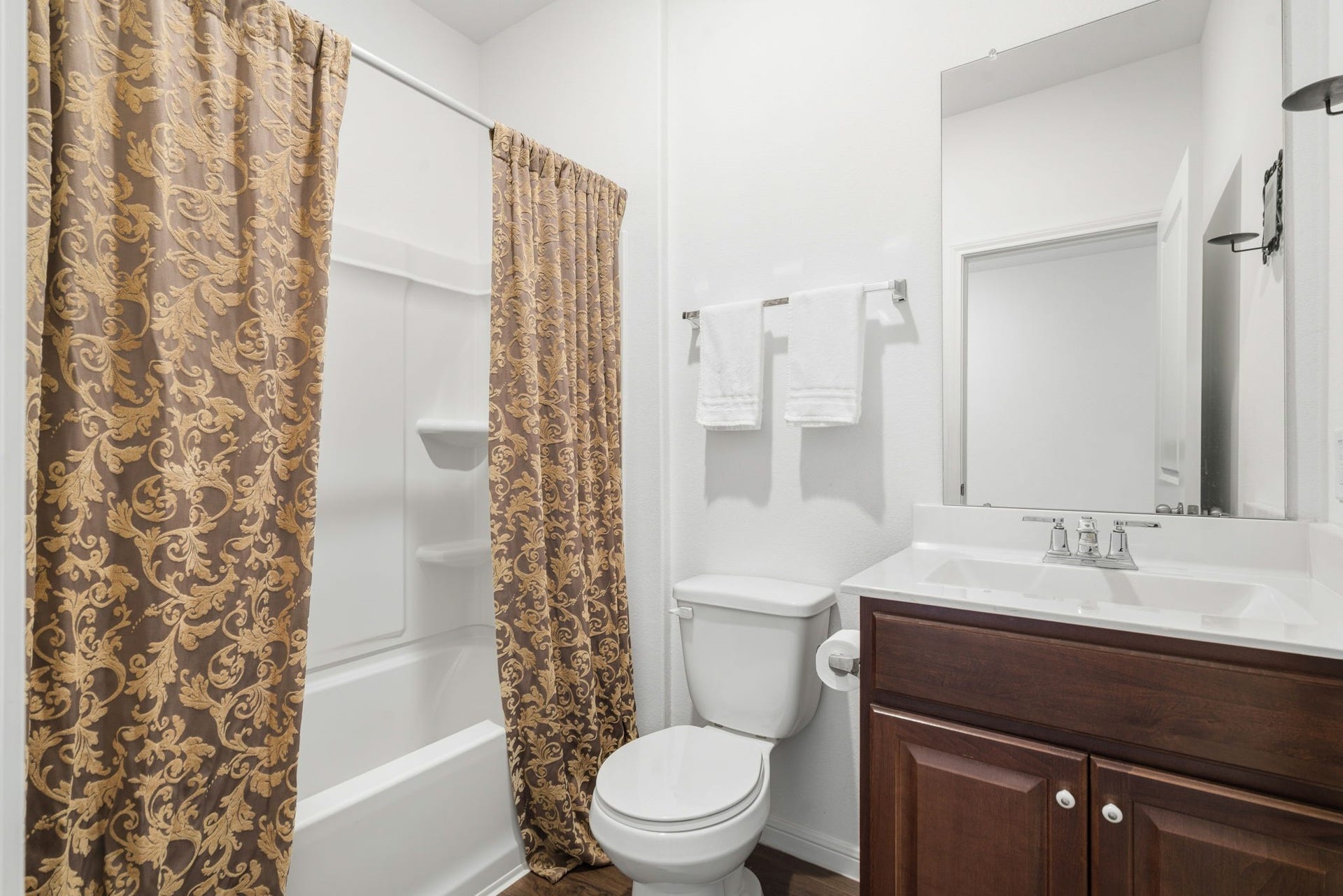 122 Ashwood Glade Lane, Conroe, TX 77378 Elegant bathroom featuring a classic shower-tub combo with ornate curtains, a sleek vanity with a polished surface, and rich wood cabinetry for a touch of warmth and sophistication.