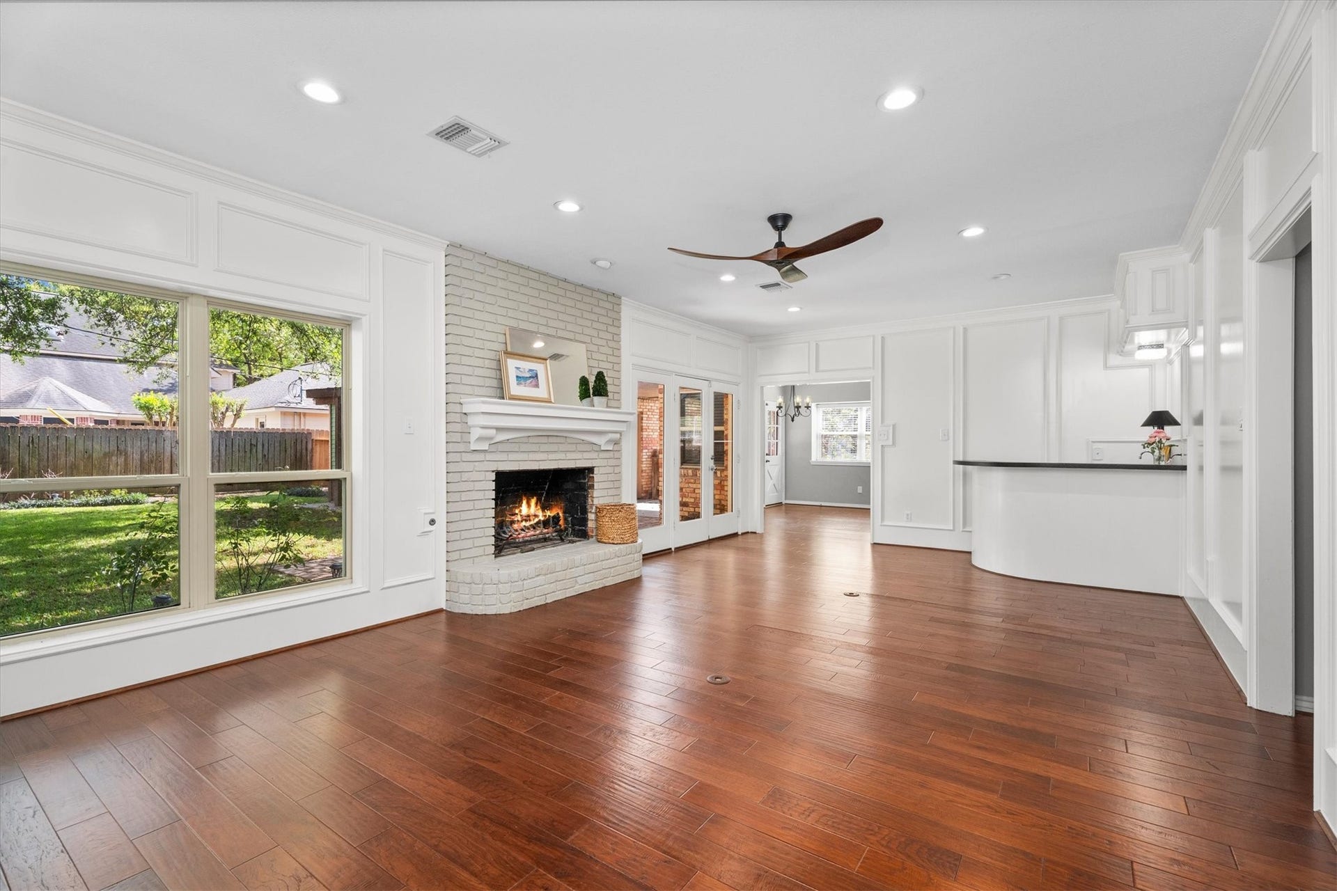 A traditional wood-burning fireplace is centered in this living room, with warm wood floors continuing throughout and a fun, curved wet bar adds interest.