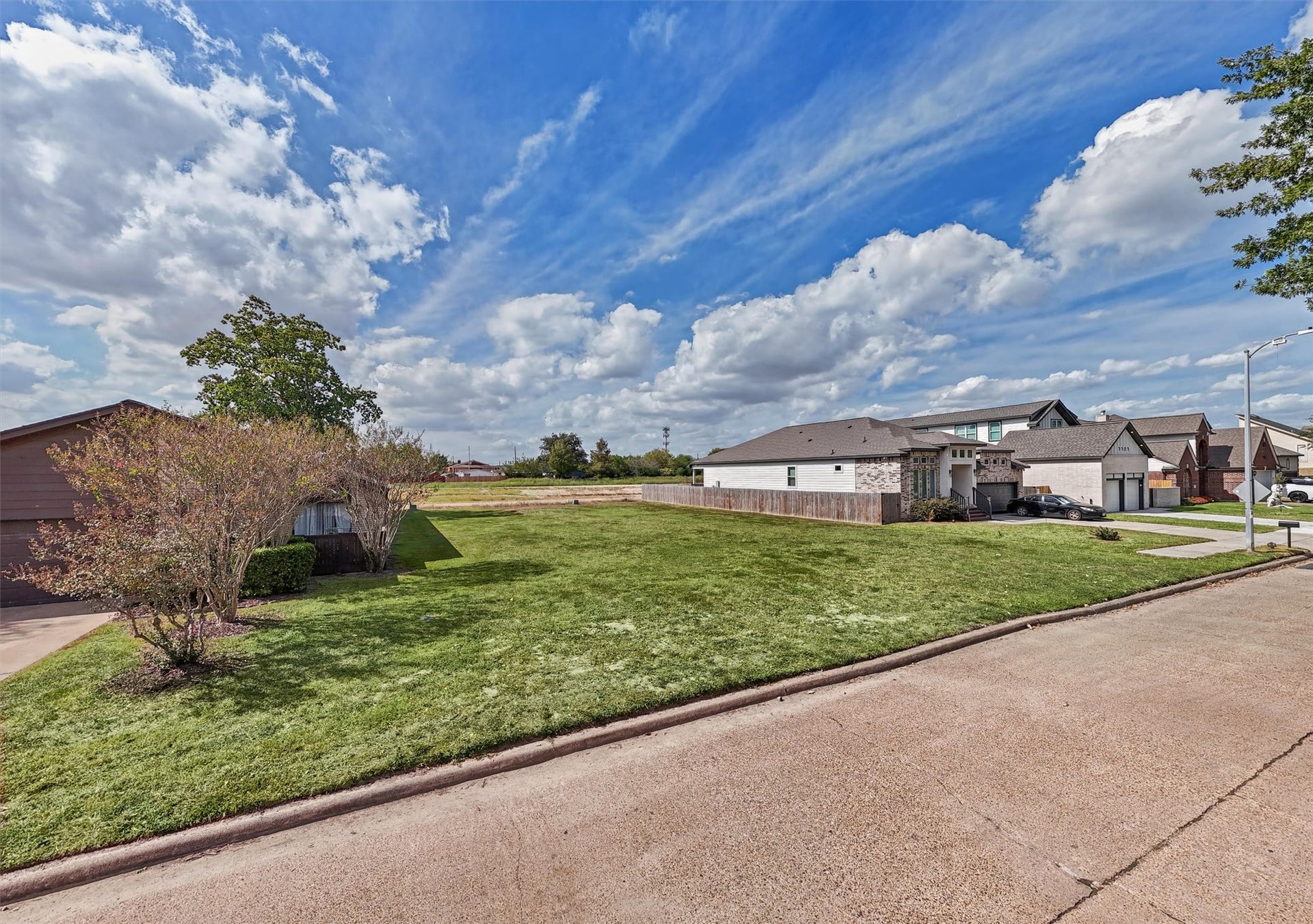 7713 Green Lawn Drive, Houston, TX 77088 YOUR DREAM HOME STARTS HERE! Imagine the possibilities with this spacious, cleared residential lot nestled among beautiful established homes! This street-level view showcases the property's generous open space, attractive neighborhood setting, and mature trees nearby.