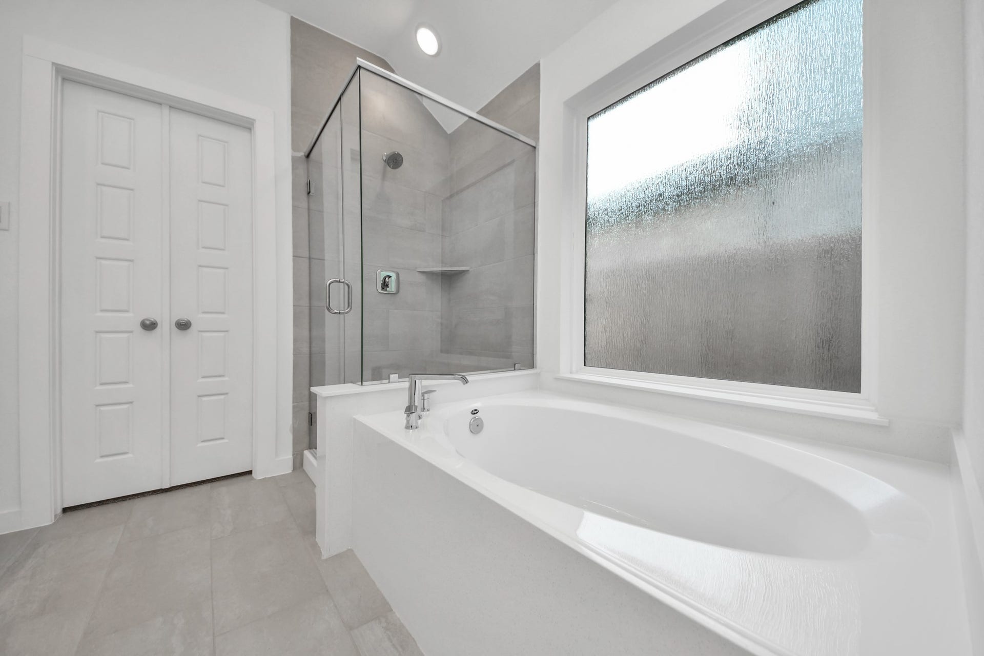 Indulge in a spa-like retreat within the confines of this primary bathroom. Delight in a spacious walk-in shower enveloped in stylish tile surround, unwind in a separate garden tub adorned with custom detailing. Sample photo of completed home with similar floor plan. Actual colors and selections may vary.