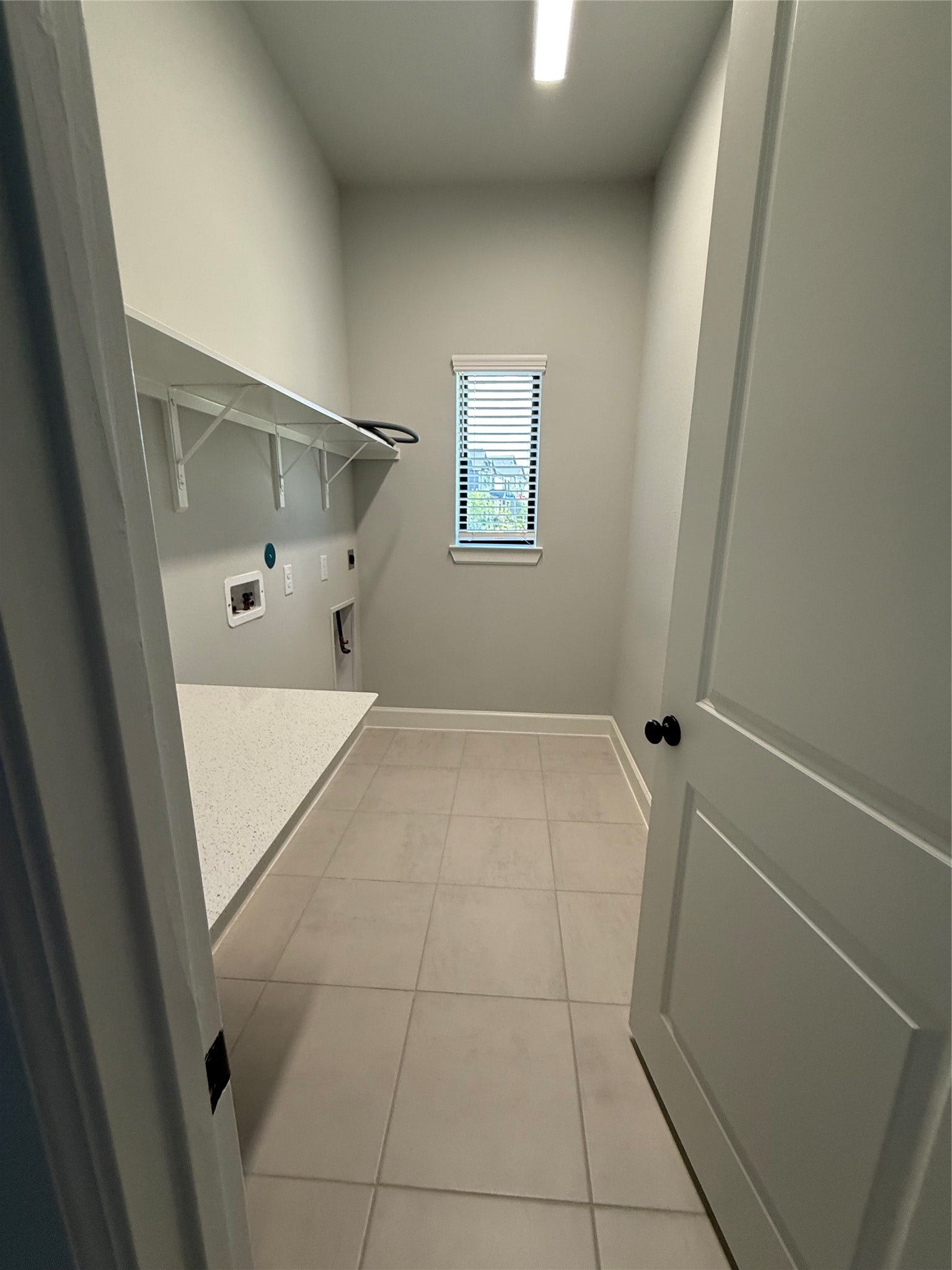 10526 William Park Drive, Missouri City, TX 77459 Bright and functional laundry room featuring sleek tile flooring, ample counter space, and convenient shelving, with a window providing natural light.