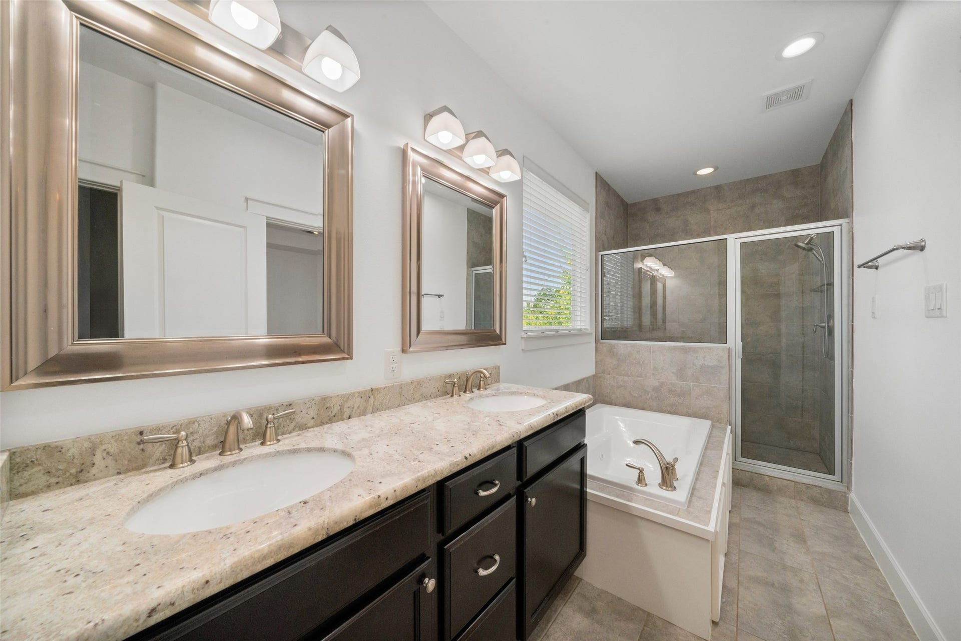 904 W 20th Street, #A, Houston, TX 77008 Your primary ensuite! This modern bathroom features dual sinks with a granite countertop, large mirrors, ample lighting, a glass-enclosed shower, and a separate jetted tub.