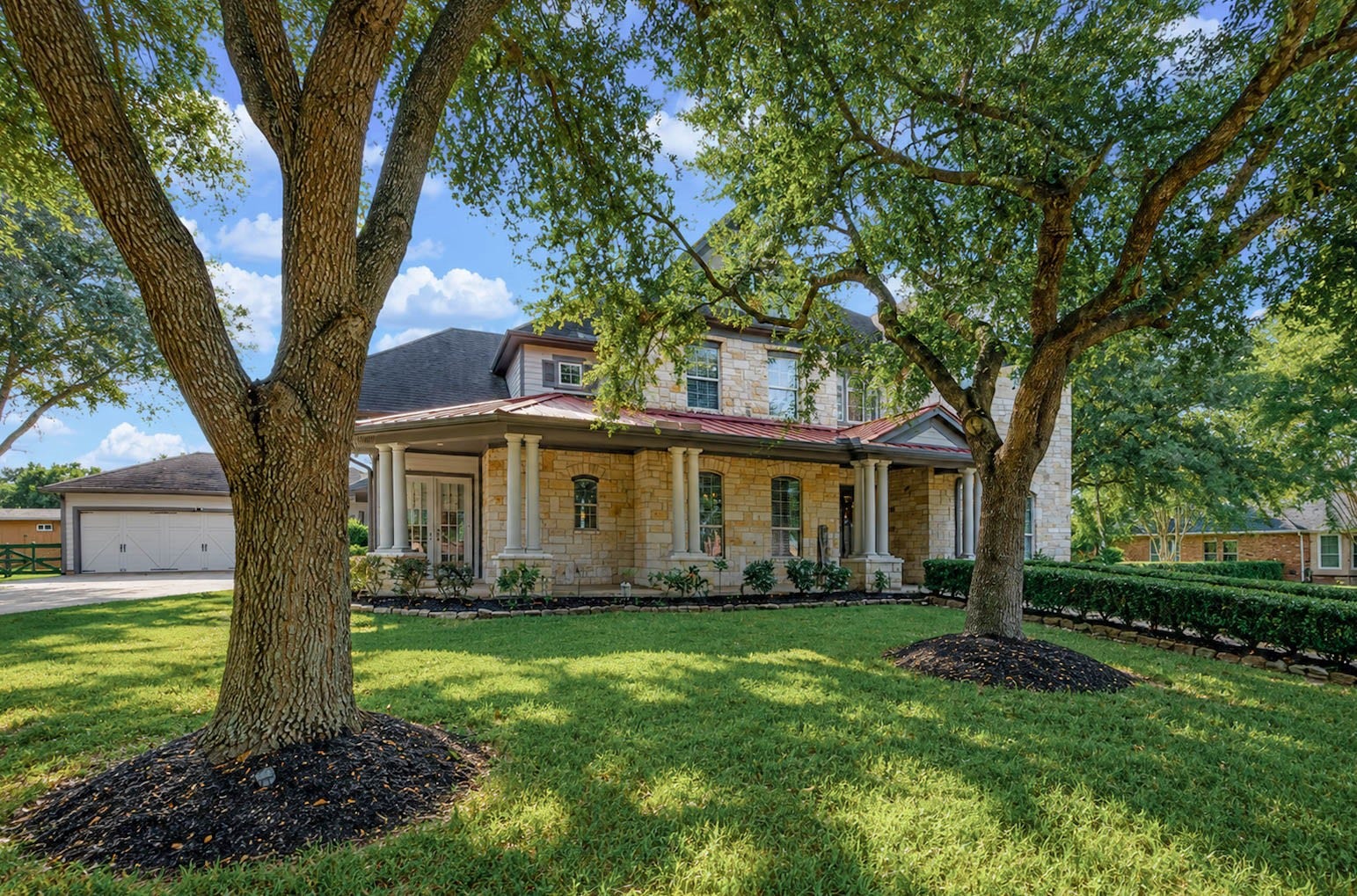 5331 W Farm Way, Fulshear, TX 77441 The exterior showcases a stunning stone elevation with an accent tin roof, and a covered wraparound front porch that is shaded by mature live oaks, adding to the charm to this home.