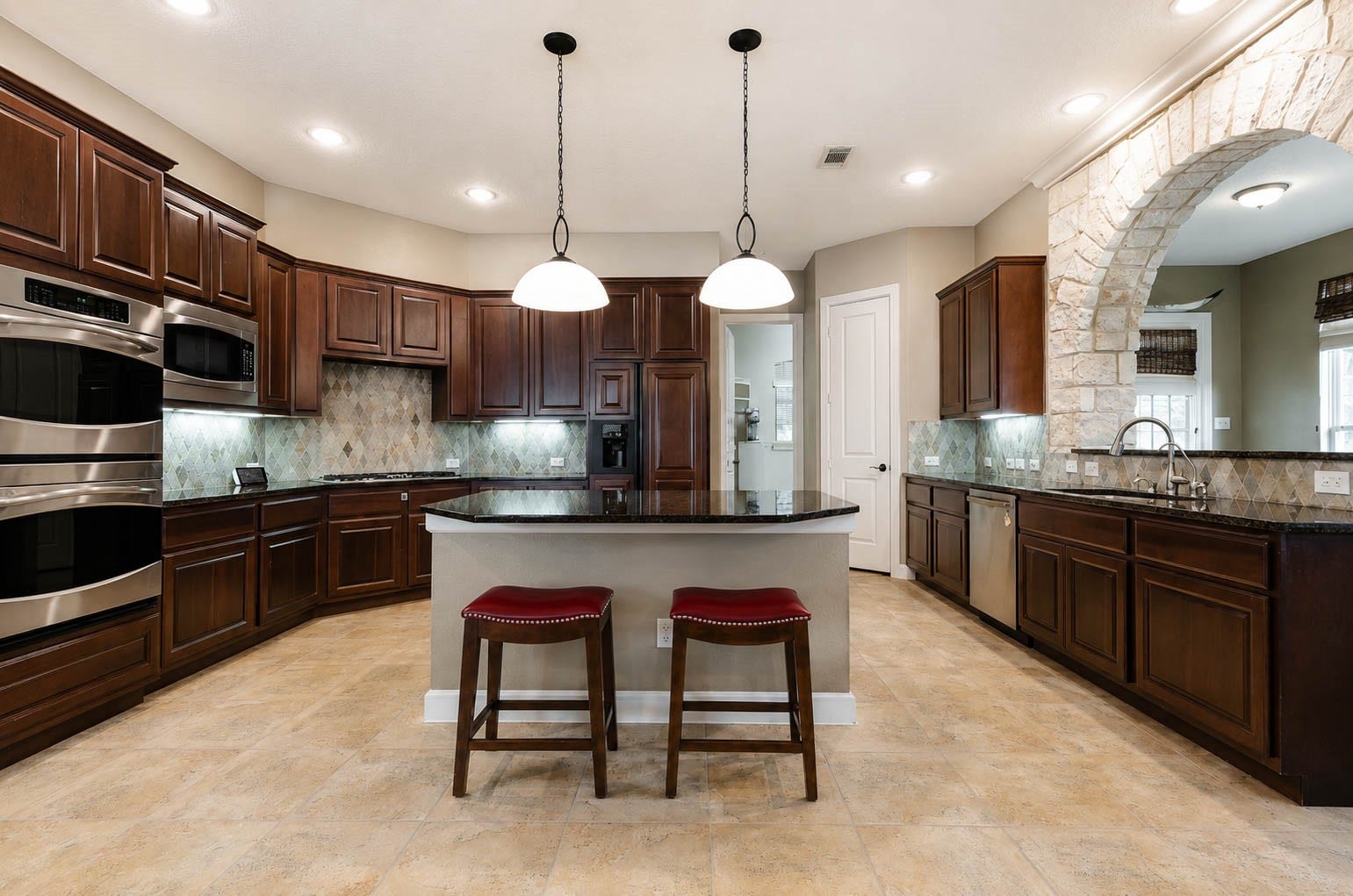 5331 W Farm Way, Fulshear, TX 77441 The heart of the home, this spacious kitchen showcases granite countertops, a tile backsplash, double ovens, and a large center island framed by one of the home's signature stone arches.