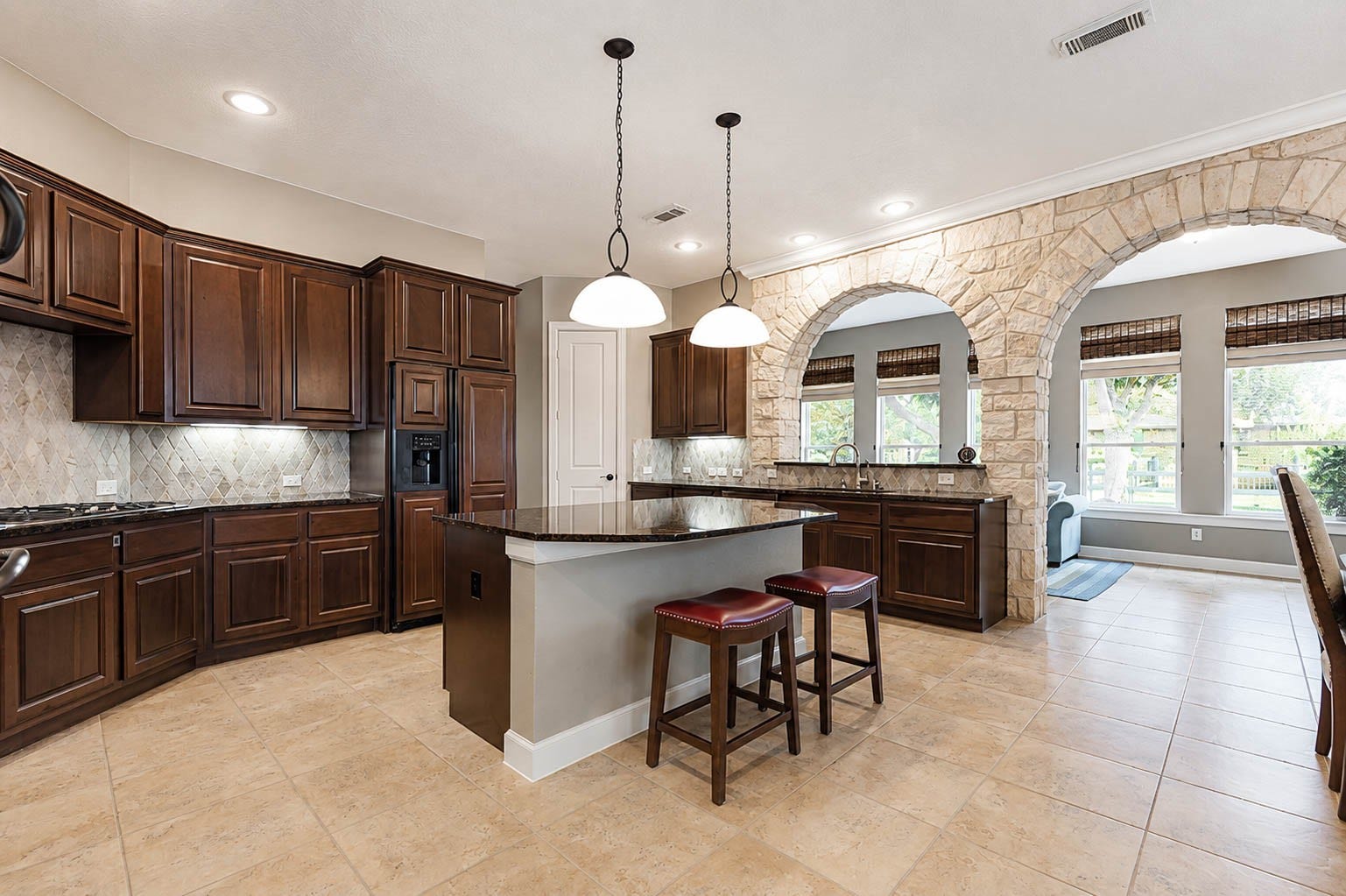 5331 W Farm Way, Fulshear, TX 77441 This kitchen has so much to offer, from the granite center island to the tile backsplash, and flows seamlessly into the sunroom through twin 10 foot stone arches that catch your eye and add architectural interest.