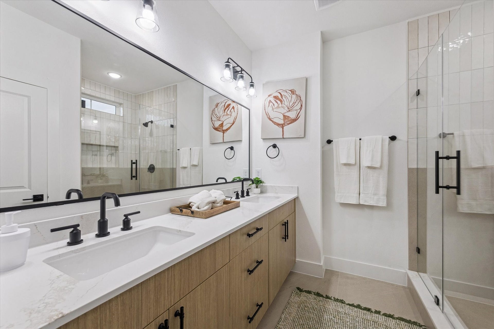 Elegant bathroom featuring a spacious double vanity with sleek black fixtures, a large mirror, and a modern glass-enclosed shower.