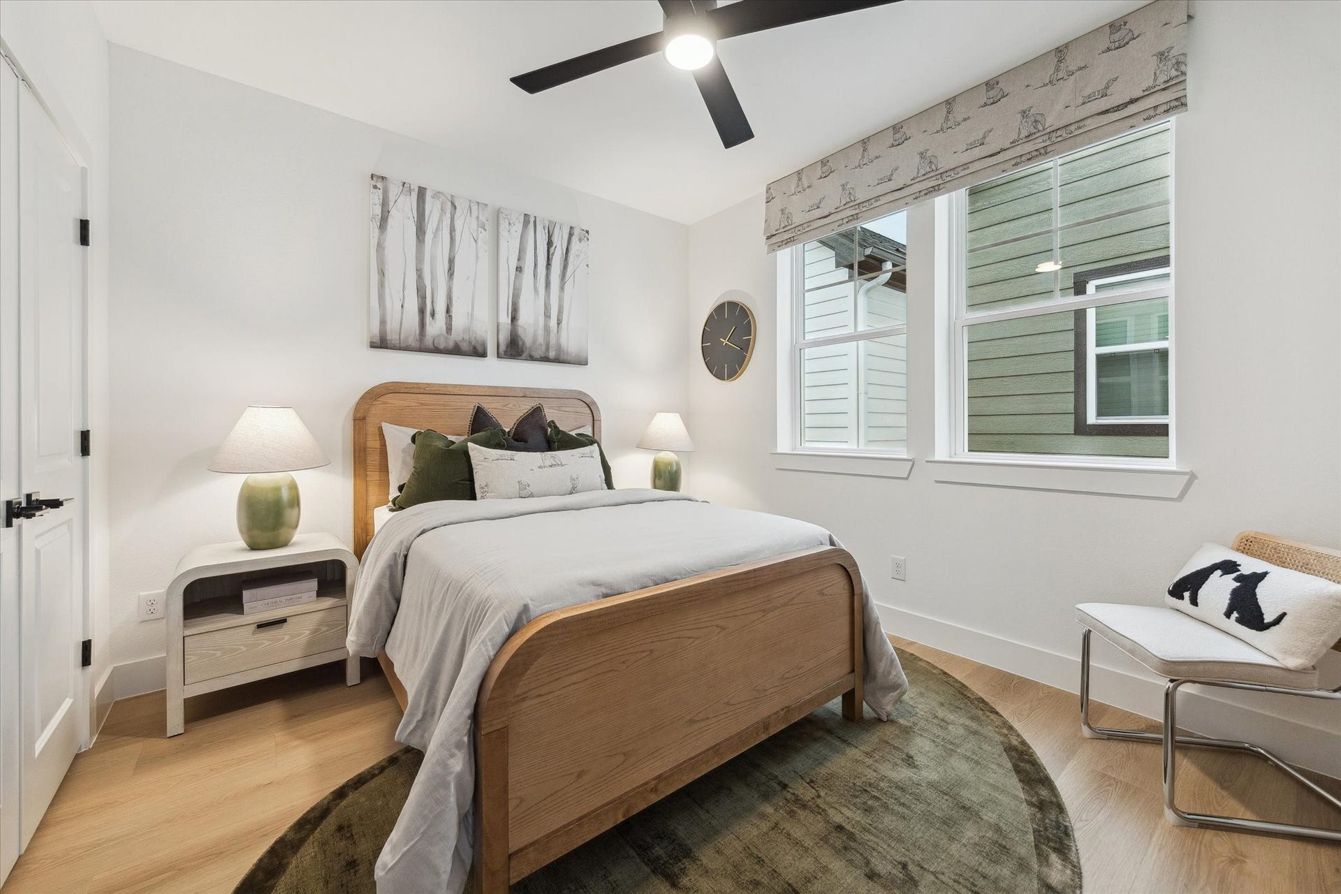 Charming bedroom with a cozy wooden bed, modern ceiling fan, and ample natural light from large windows, complemented by tasteful decor and a serene color palette.