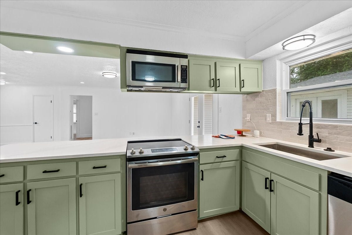 11510 Mullins Drive, Houston, TX 77035 Modern kitchen featuring sleek appliances, soft green cabinetry, and ample counter space, all bathed in natural light from a large window.