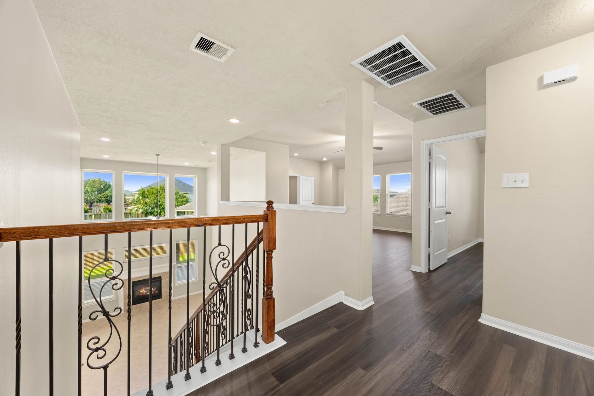 Come upstairs to a spacious landing that seamlessly connects the home's second-level retreat. Rich dark wood flooring spans this open corridor, which features an elegant wrought-iron railing overlooking the family room below, while offering a clear view into the adjacent, sunlit game room and the hallway leading to the private secondary bedrooms.