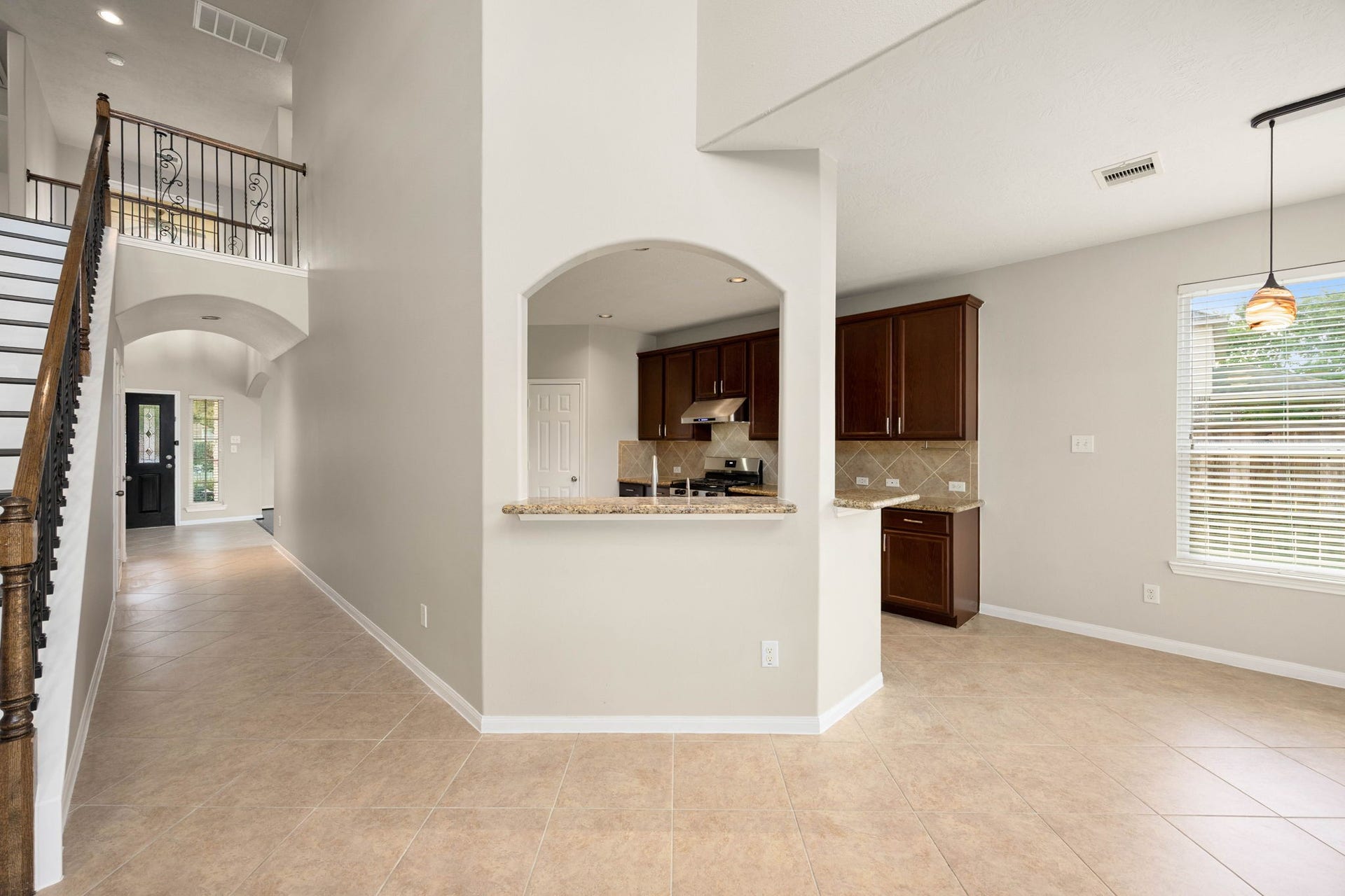 An elegant arched pass-through window creates a seamless visual connection between the kitchen and the central family room, keeping the home feeling bright and integrated. This unique architectural detail frames the rich dark cabinetry, granite countertops, and tiled backsplash of the kitchen while preserving the distinct spaces of the main floor layout.