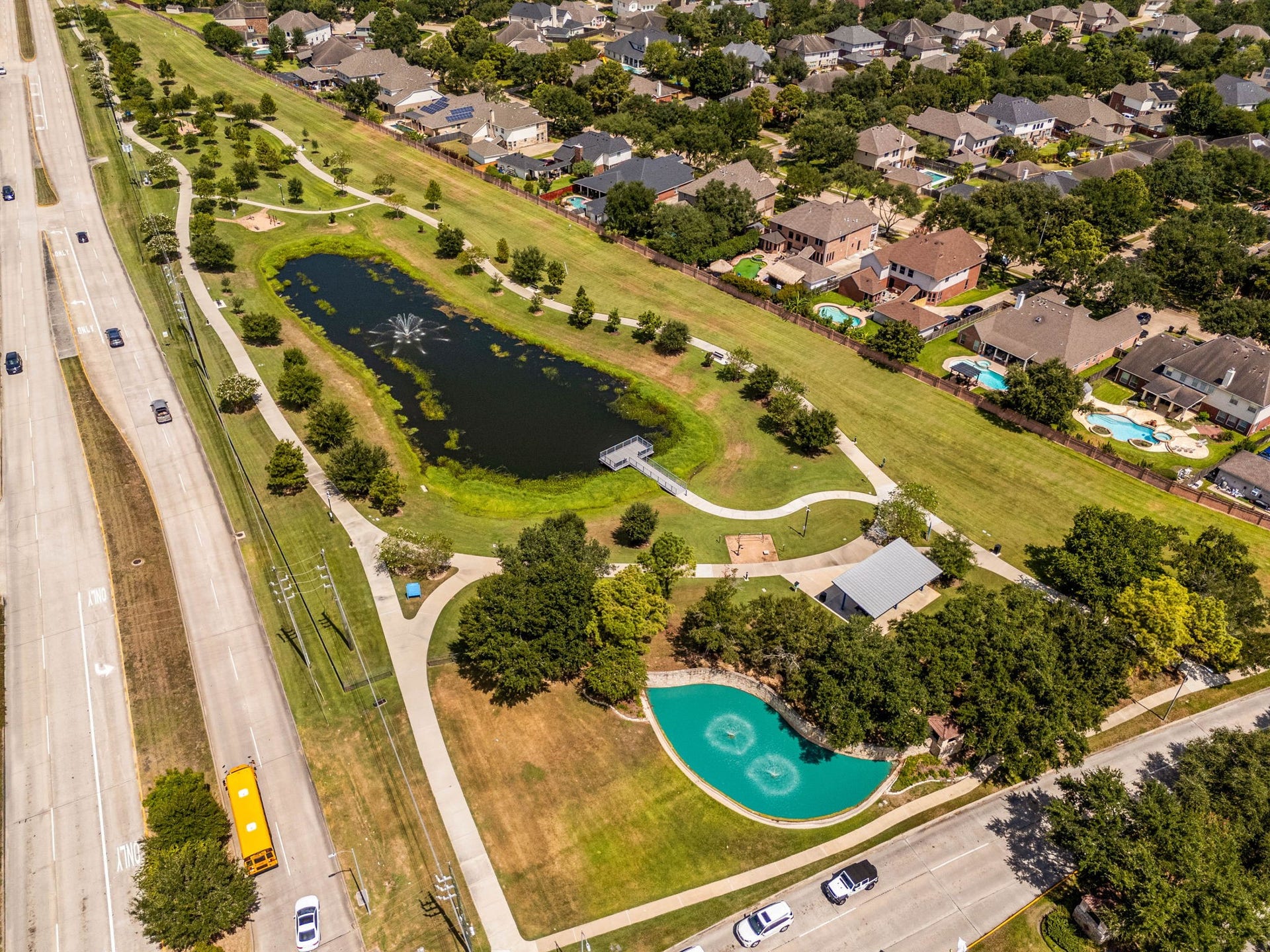 Embrace an active outdoor lifestyle with the scenic green spaces located right inside Katy Creek Ranch. This aerial view showcases the neighborhood's beautiful central park, which features a tranquil walking trail winding past a fountain-centered lake, a covered community pavilion, a dedicated playground area, and a peaceful fishing pier perfect for relaxing afternoons.