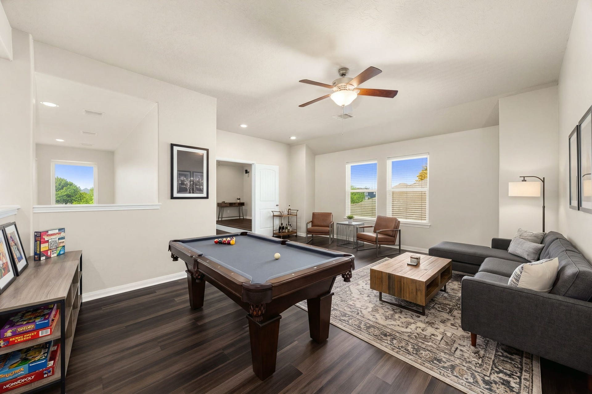 This massive upstairs game room offers endless possibilities for entertainment, recreation, or a quiet study loung. The sprawling space features rich dark flooring, a modern ceiling fan, and multiple large windows that keep the area bright and open, while a half-wall cutout provides a visual connection to the grand staircase and lower-level living areas. *Virtually Staged