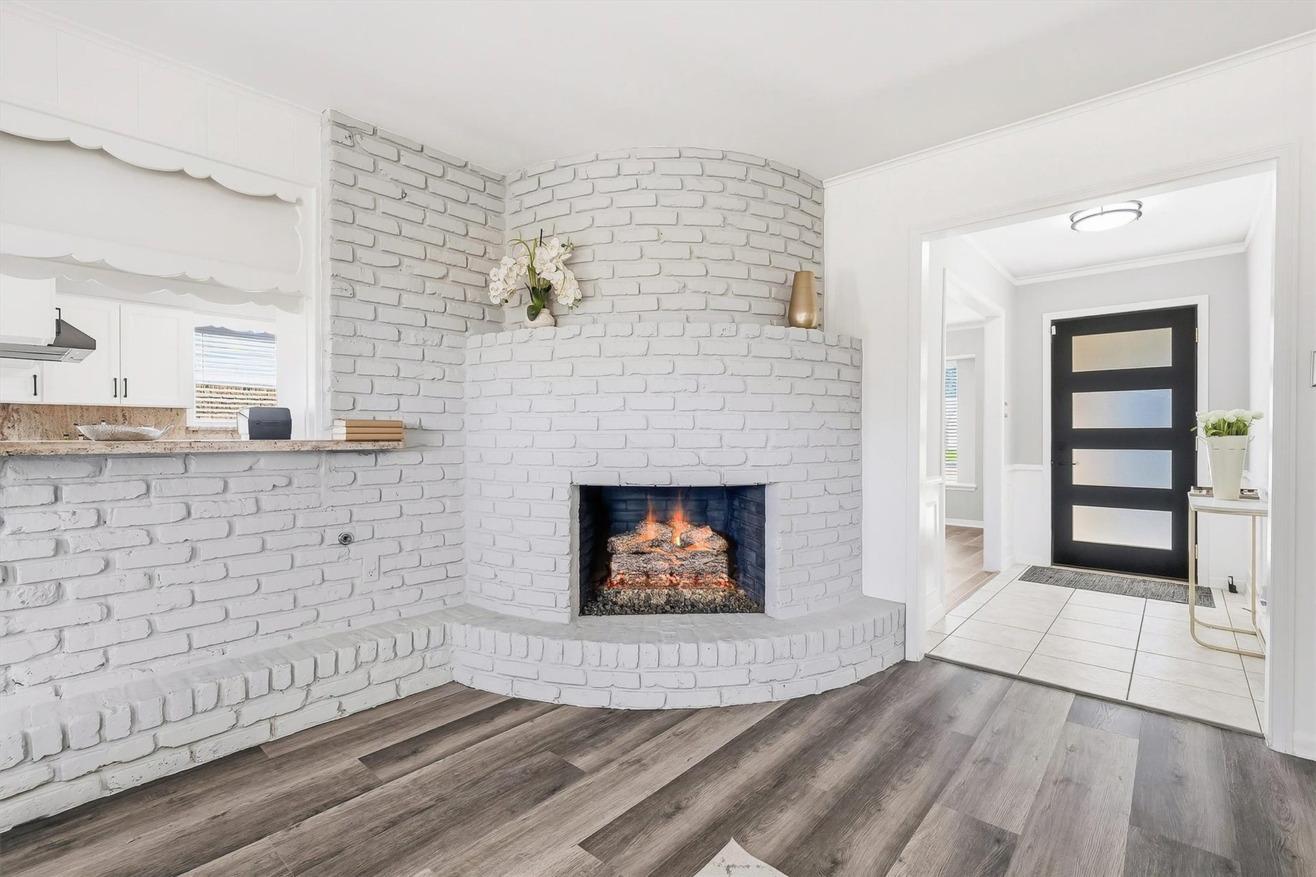 2503 Moss Hill Drive, Houston, TX 77080 Charming living area features a whitewashed brick fireplace, complemented by sleek vinyl plank flooring and a modern black front door.