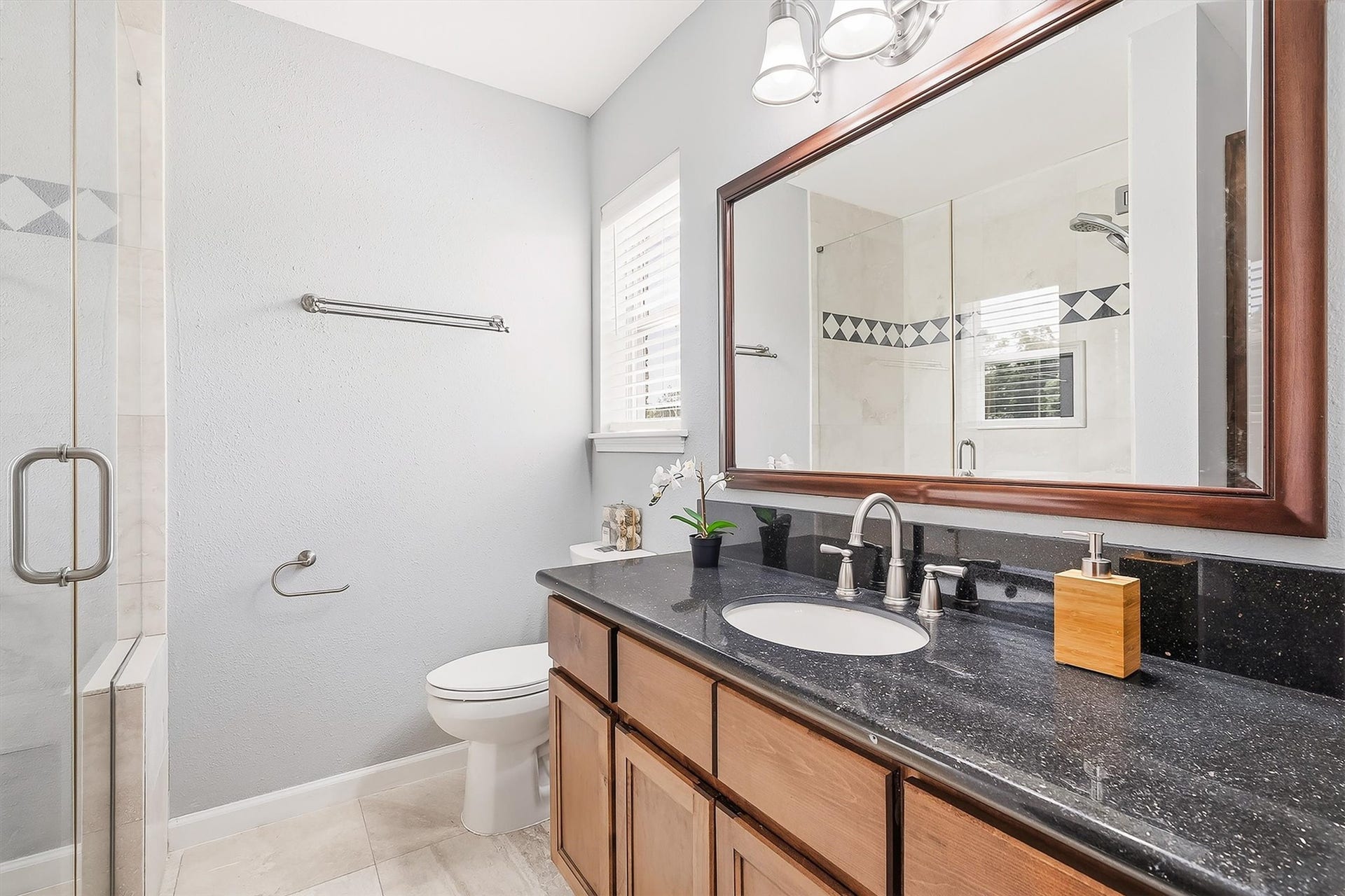2503 Moss Hill Drive, Houston, TX 77080 Elegant primary bathroom featuring a sleek black granite countertop, double sink vanity, and a spacious glass-enclosed shower with decorative tile accents.